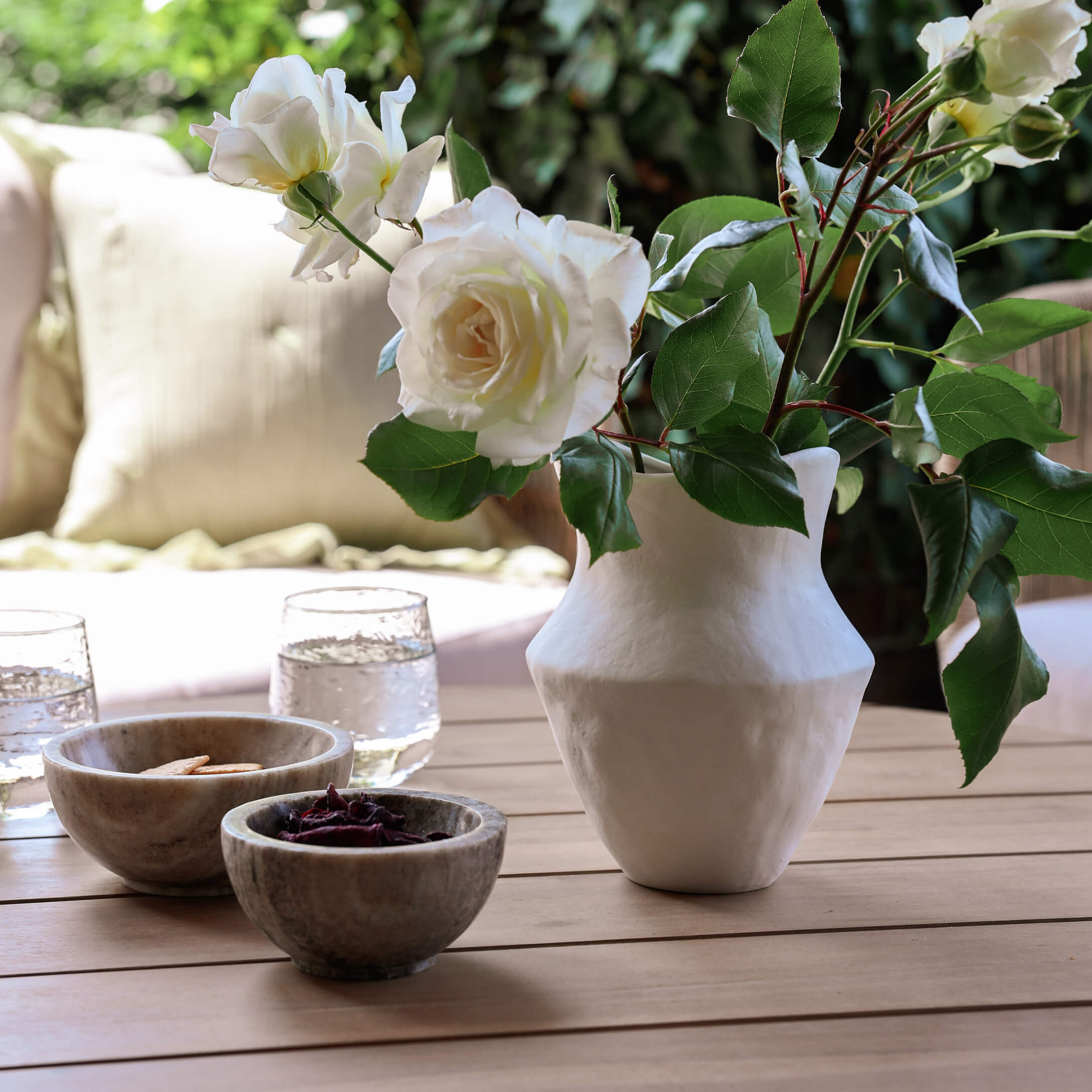 Weisse Keramikvase mit weissen Rosen auf Holztisch mit Schalen und Wassergläsern