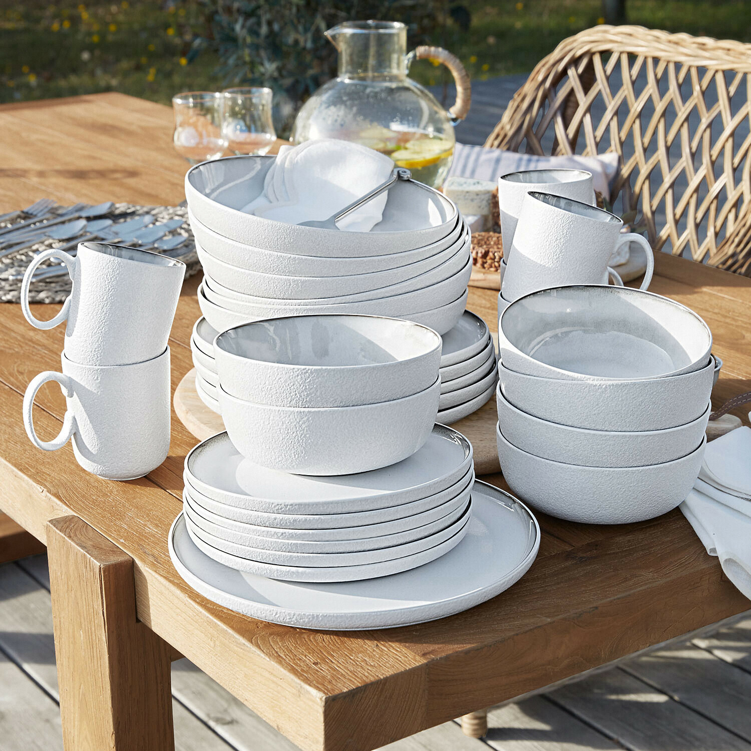 Weisses, strukturiertes Keramik-Geschirrset auf Holztisch im Aussenbereich gestapelt