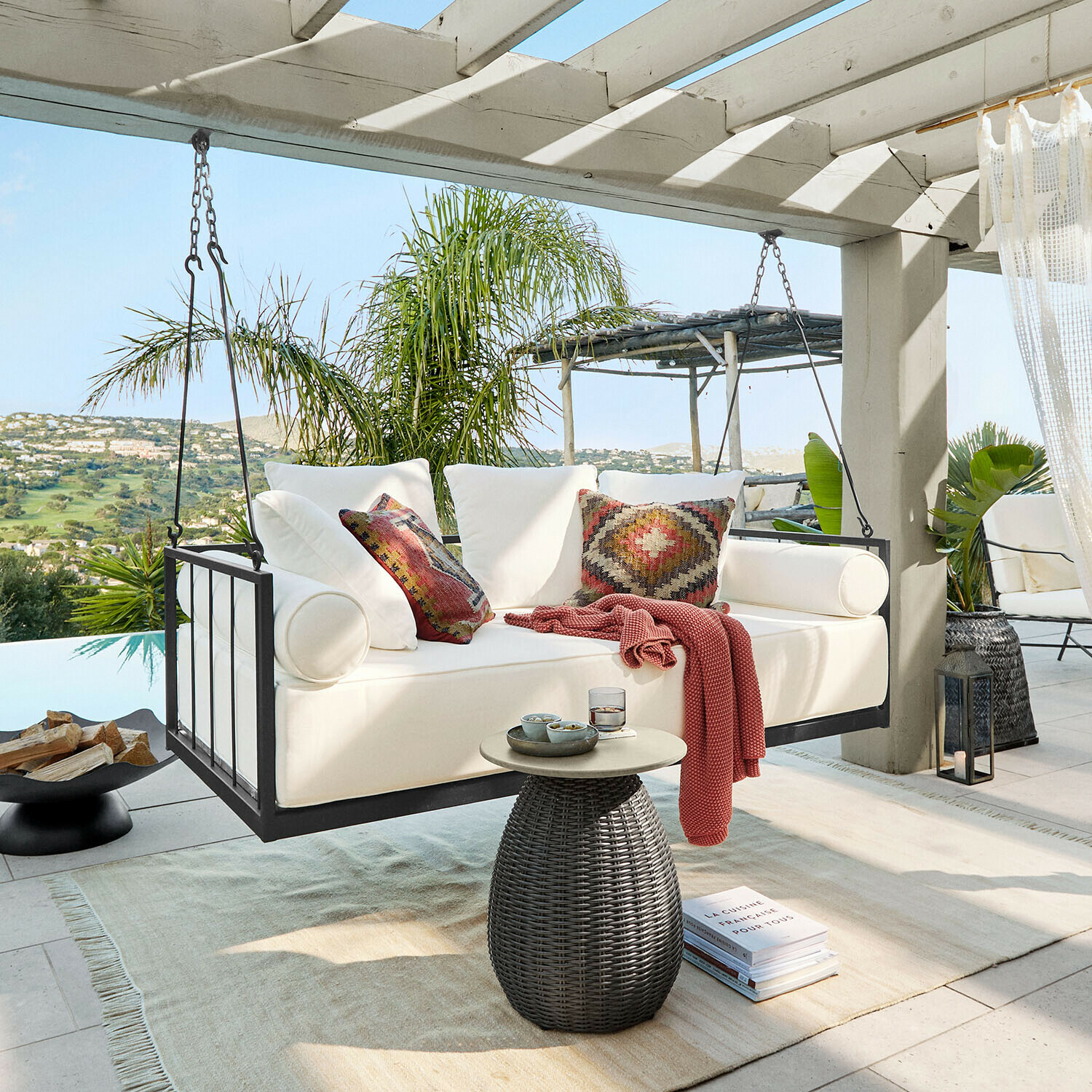 Hängebank Bellecôtes Weisse Hängesofa mit Metallrahmen und bunten Kissen auf Terrasse mit grünem Ausblick