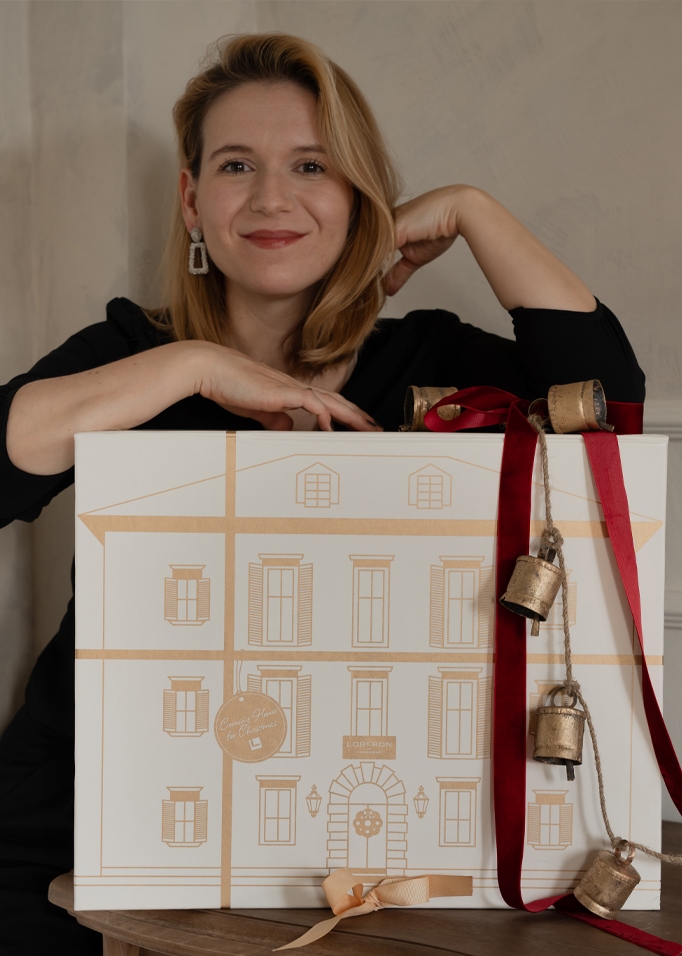 Frau mit Geschenkbox in Weiss mit goldenem Hausdruck und roten Glocken an Schnur als Adventsdekoration