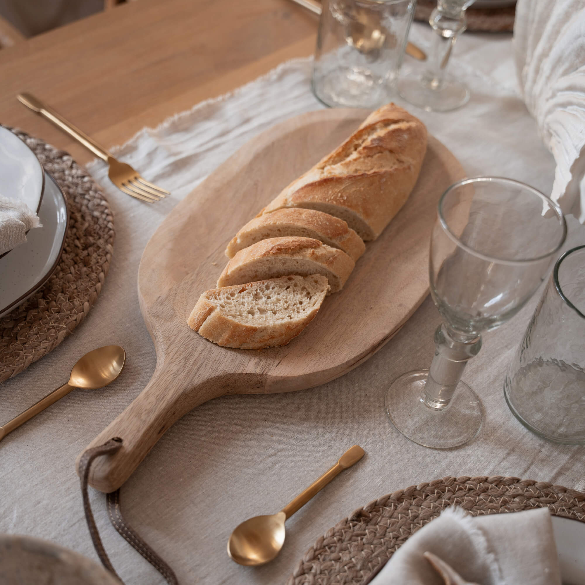 Holzschneidebrett mit aufgeschnittenem Baguette auf Tisch mit Geschirr und goldenen Bestecken