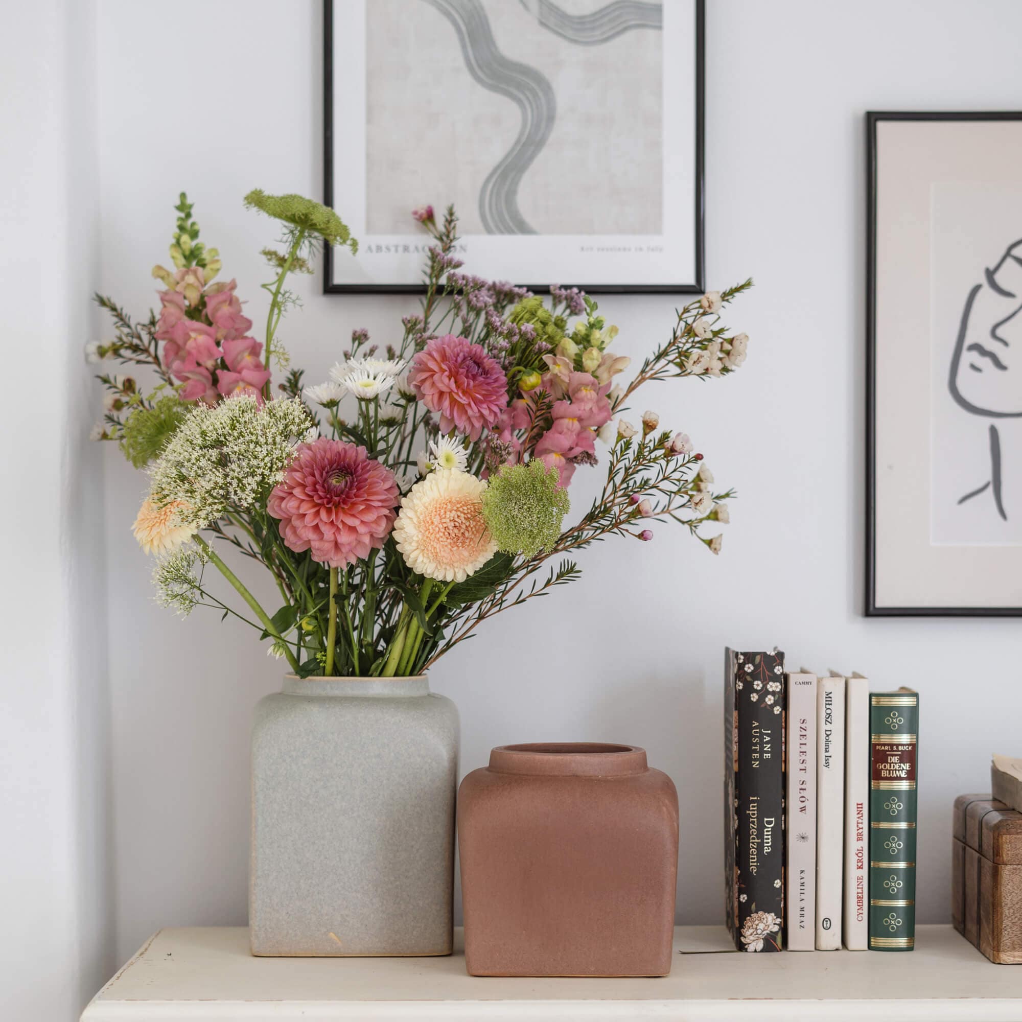 Zwei keramische Vasen in Grau und Braun auf einem weissen Tisch mit Blumenstrauss und Büchern