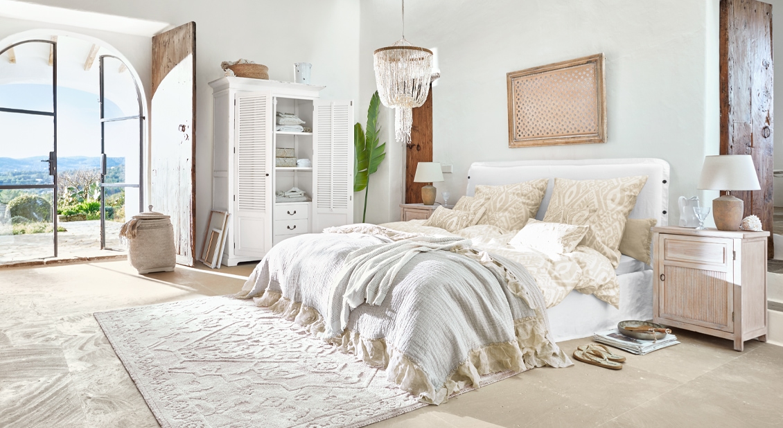 Helles Schlafzimmer mit weissem Bett, beiger Bettwäsche und rustikalen Holzmöbeln