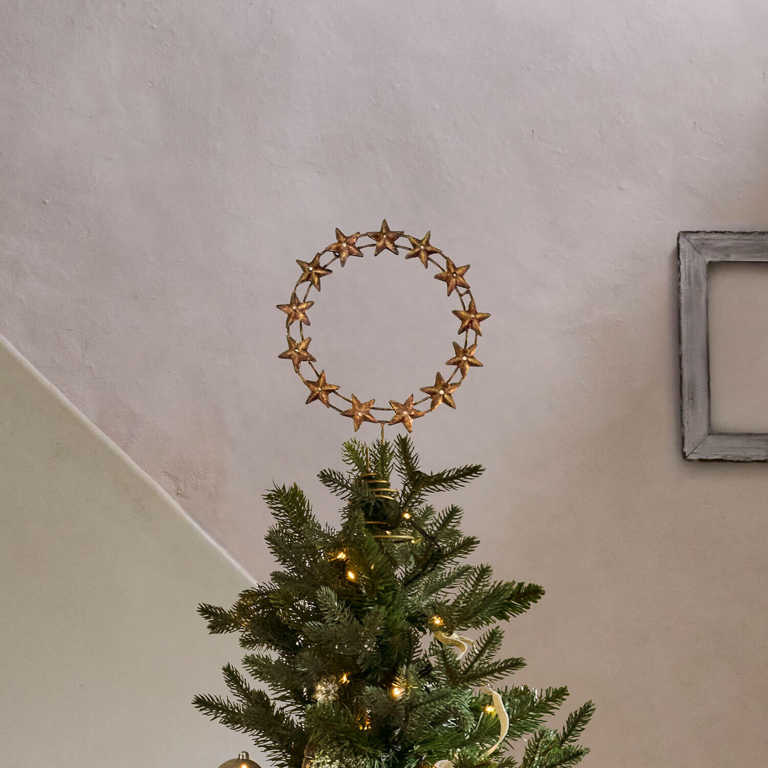 Weihnachtsbaumspitze Tavelle Goldene Sternkranz-Dekoration auf der Spitze eines grünen Weihnachtsbaums mit Lichterkette