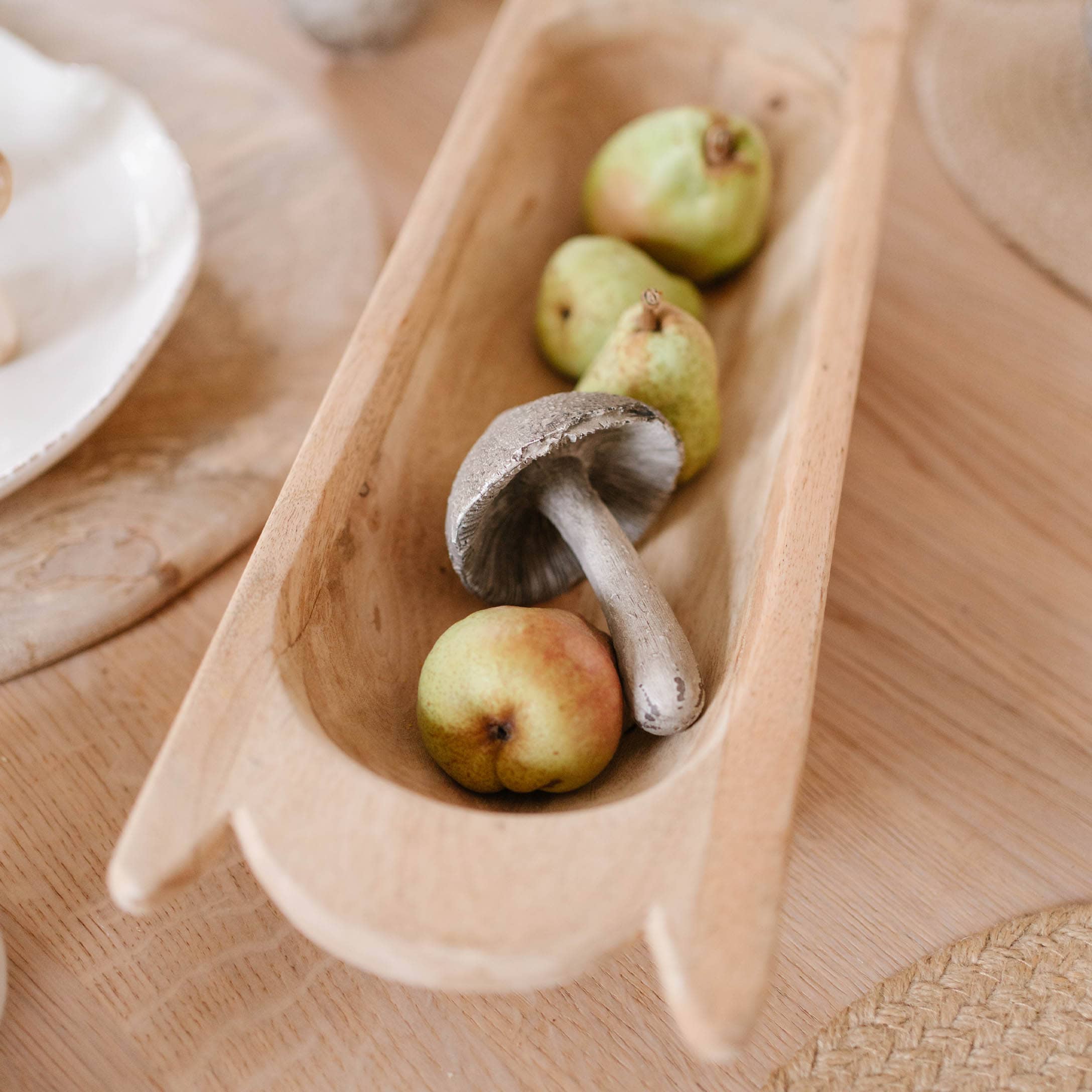 Holzschale mit dekorativem Pilz und grünen Birnen als herbstliche Tischdekoration