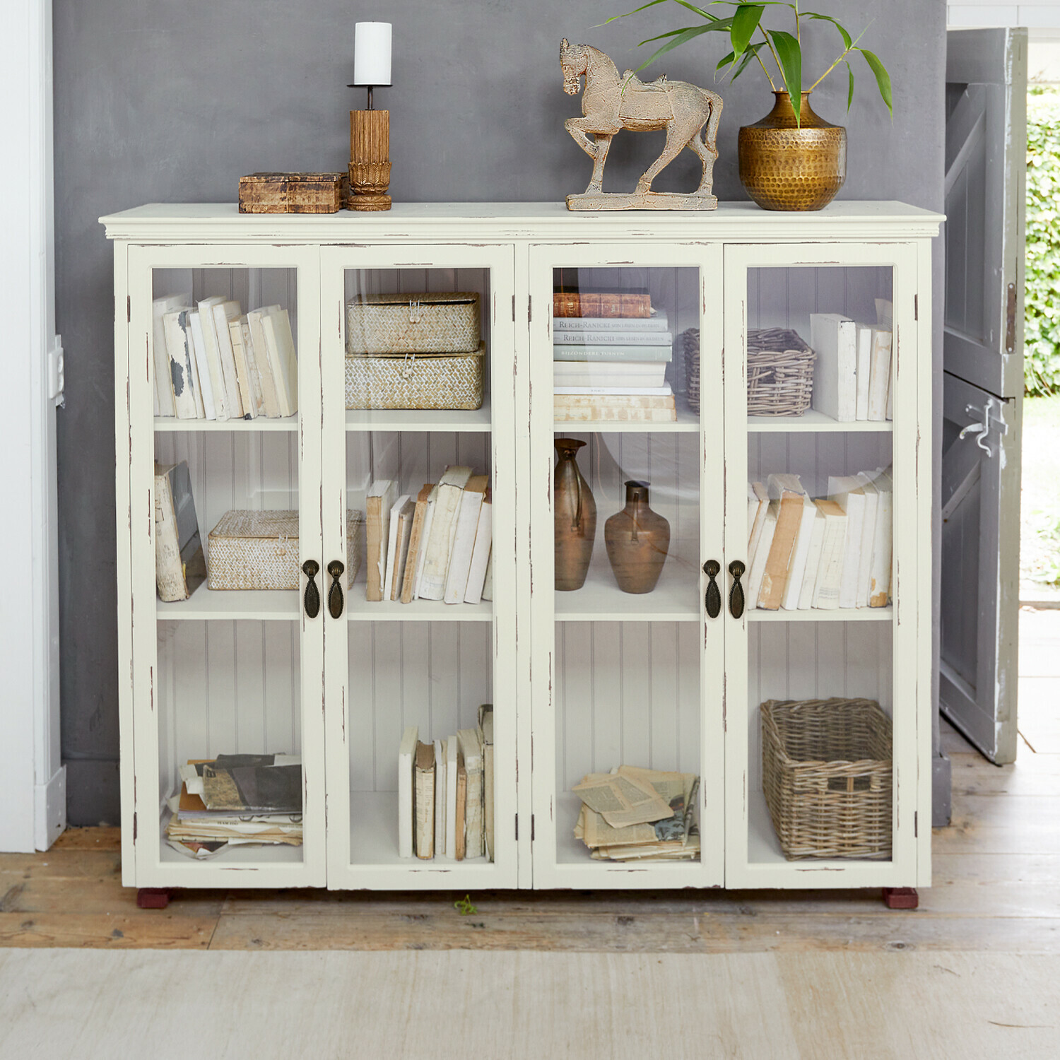 Schrank Eastbridge Weisse Holzvitrine mit Glastüren, dekoriert mit Büchern und Vintage-Objekten im Landhausstil