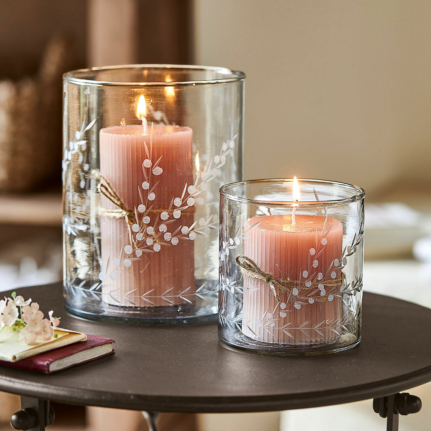 Windlicht 2er Set Temao Zwei rosa Kerzen in transparenten Glaswindlichtern mit weissem Pflanzenmuster auf einem Tisch