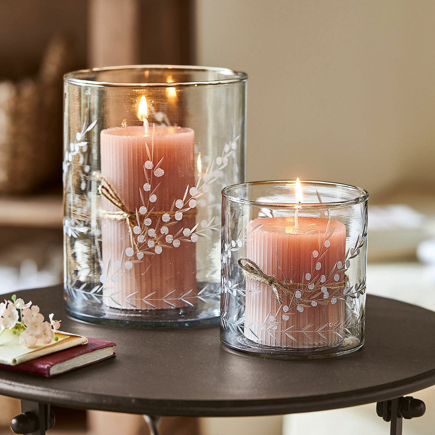 Windlicht 2er Set Temao Zwei rosa Kerzen in transparenten Glaswindlichtern mit weissem Pflanzenmuster auf einem Tisch