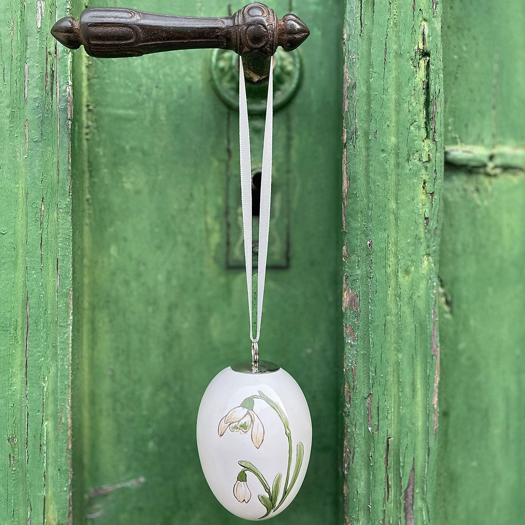 Weisse Keramik-Ostereier-Dekoration mit Blumenmotiv, an grünem Türgriff hängend