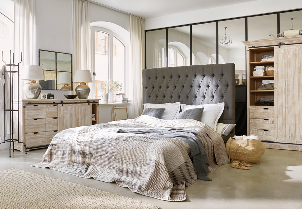 Gemütliches Schlafzimmer mit grauem, gepolstertem Kopfteil und hellen Holzmöbeln im Loft-Stil