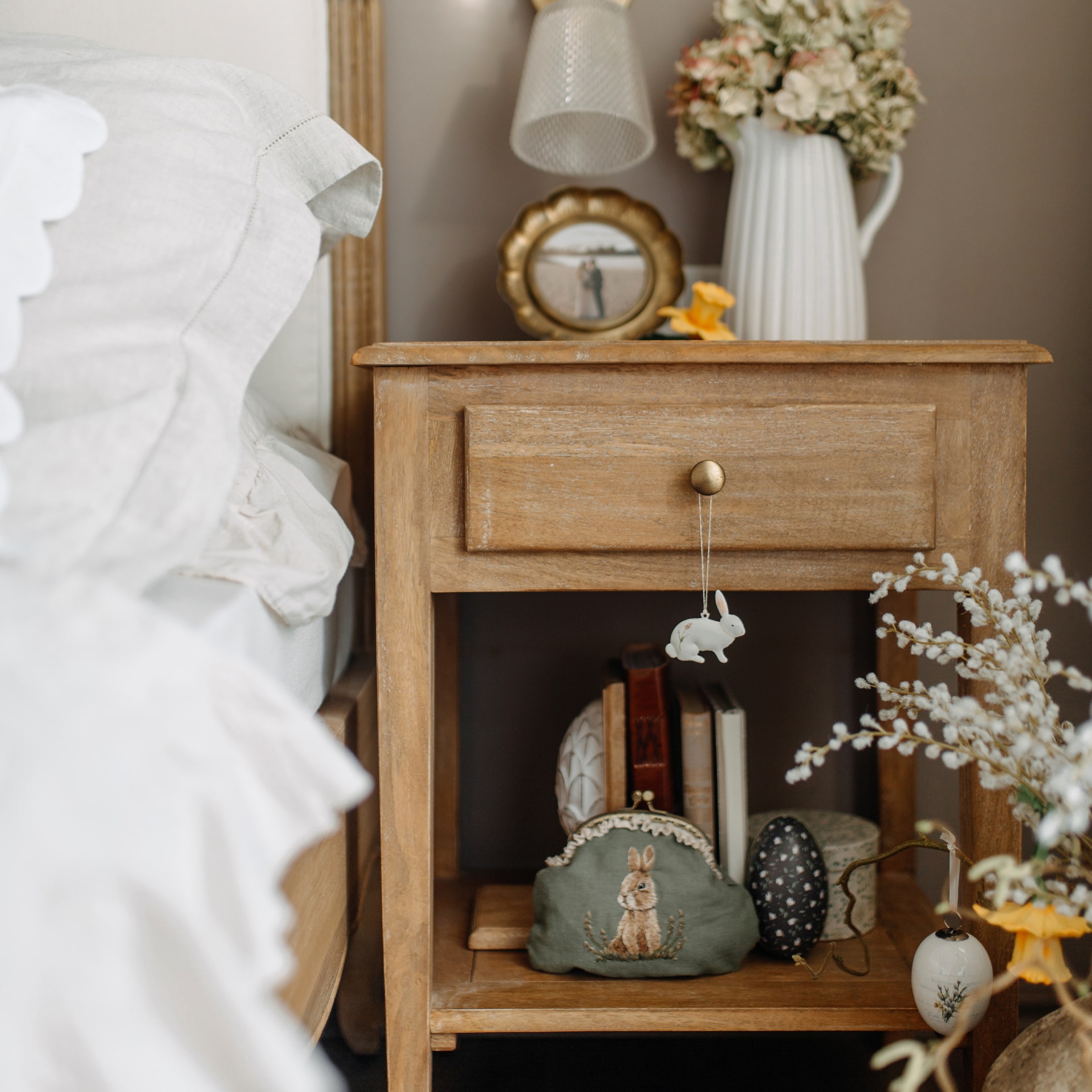 Holz-Nachttisch mit Osterdekorationen und grüner Kosmetiktasche mit Hasenmotiv im Schlafzimmer