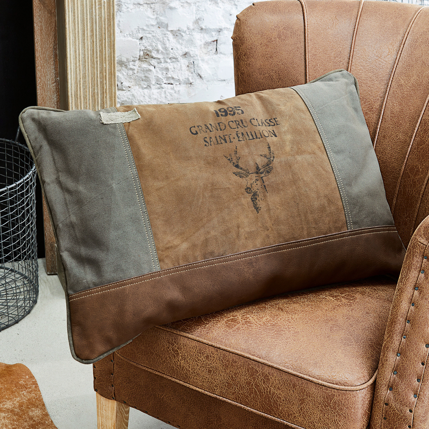Kissen Chiron Braun-graues Dekokissen mit Hirschmotiv auf braunem Lederstuhl im Vintage-Stil