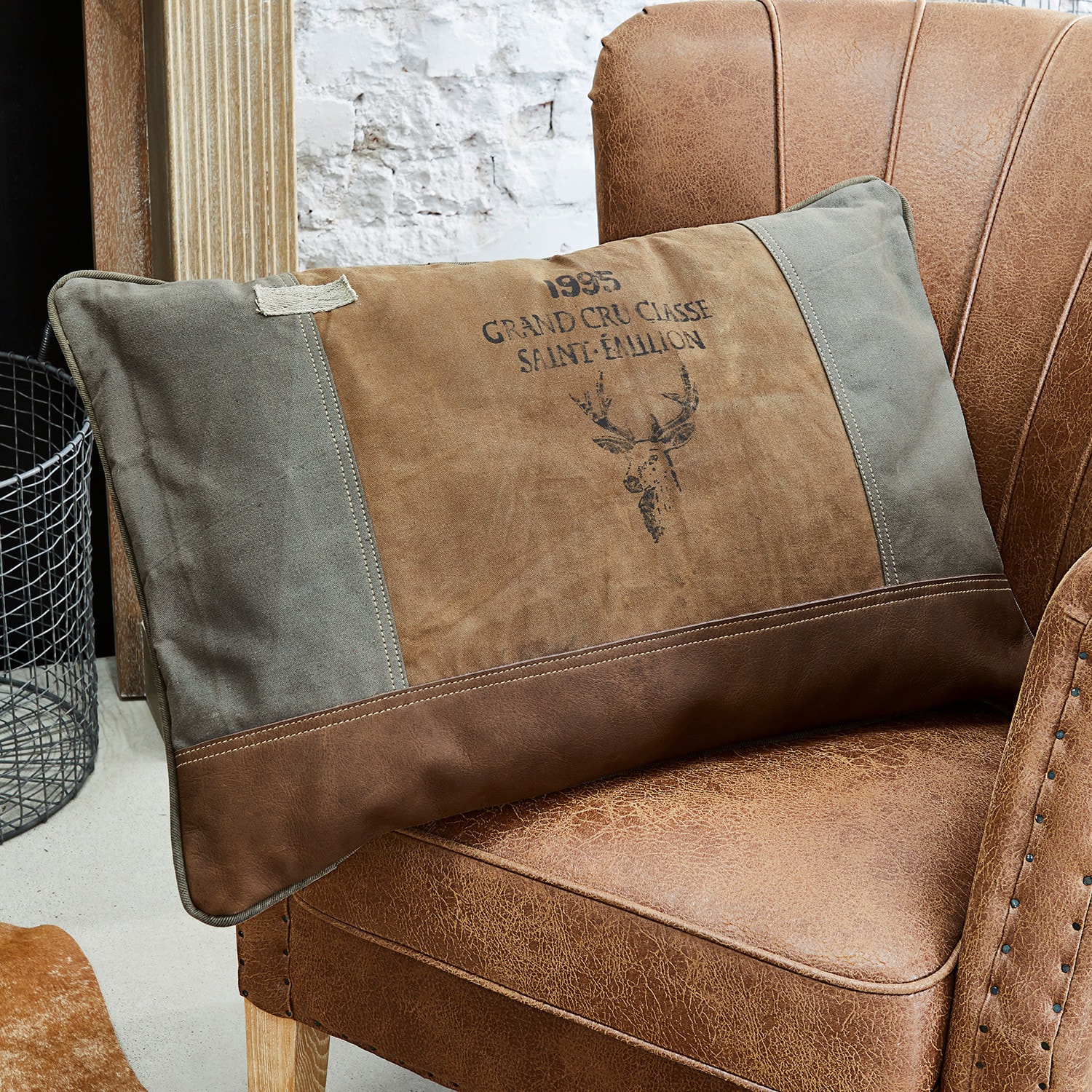 Kissen Chiron Braun-graues Dekokissen mit Hirschmotiv auf braunem Lederstuhl im Vintage-Stil