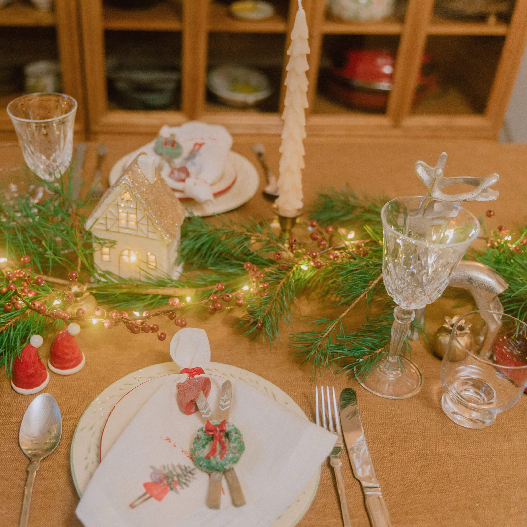 Weihnachtlich gedeckter Tisch mit grünen Zweigen, Kerzen und Kristallgläsern für festliche Stimmung.