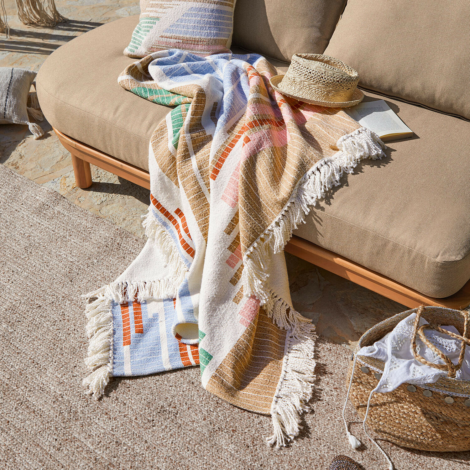 Bunte Baumwolldecke mit Fransen auf beigem Sofa im Aussenbereich, dekorativ und gemütlich