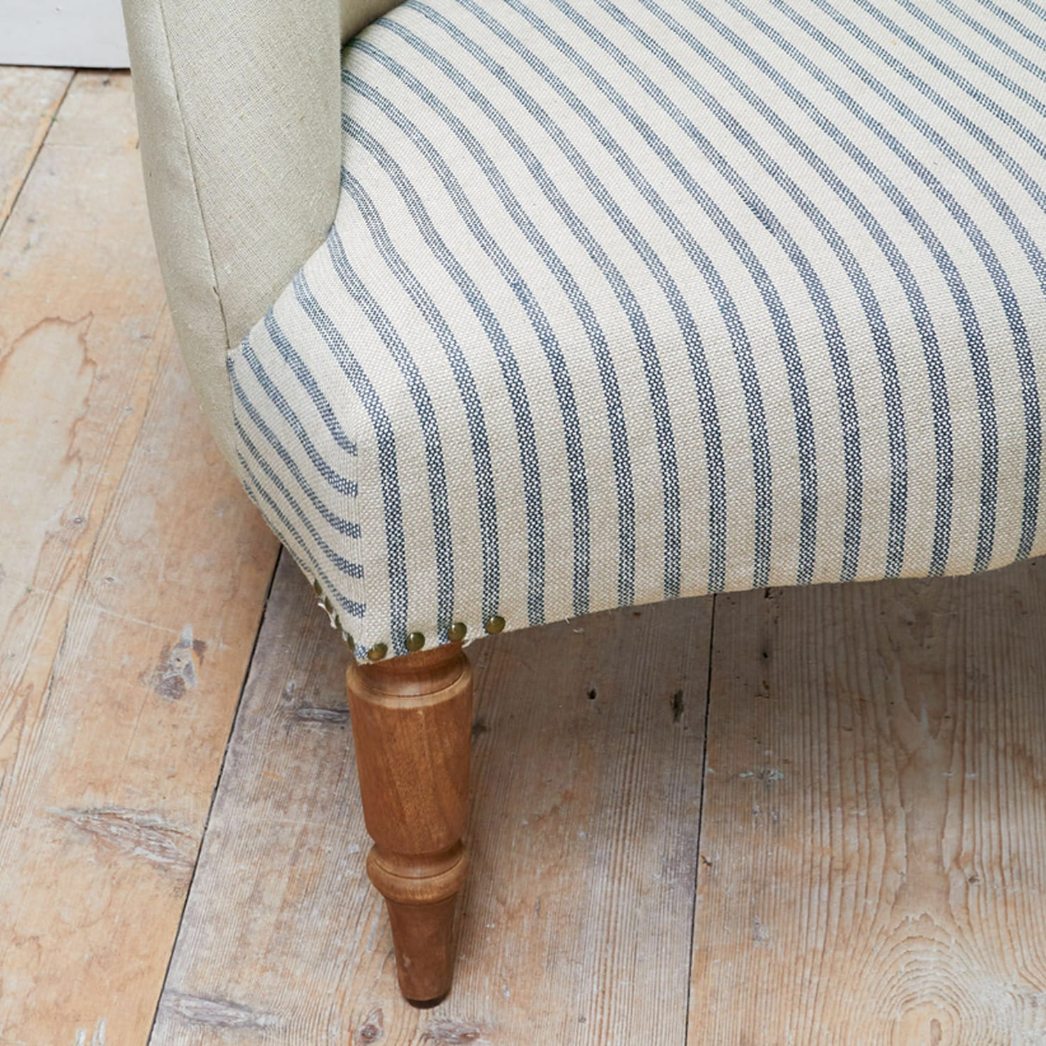 Holzbein eines Möbels mit beige-blau gestreiftem Stoffbezug auf Holzboden