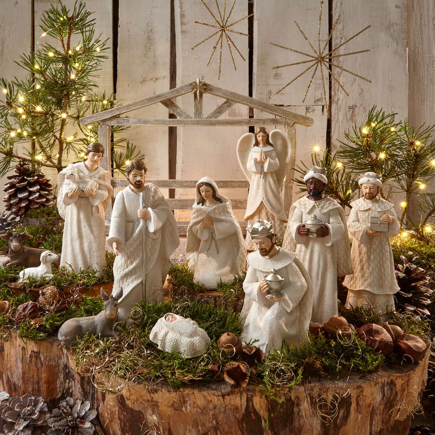 Krippenfiguren 12er Set Santo Weisses Krippenfiguren-Set aus Holz und Stoff auf natürlichem Moos- und Lichterhintergrund zur Weihnachtsdekoration