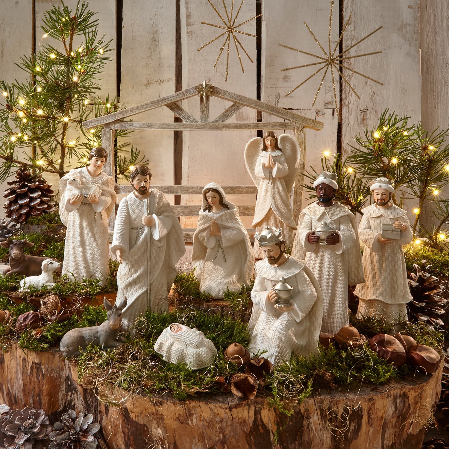 Krippenfiguren 12er Set Santo Weisses Krippenfiguren-Set aus Holz und Stoff auf natürlichem Moos- und Lichterhintergrund zur Weihnachtsdekoration