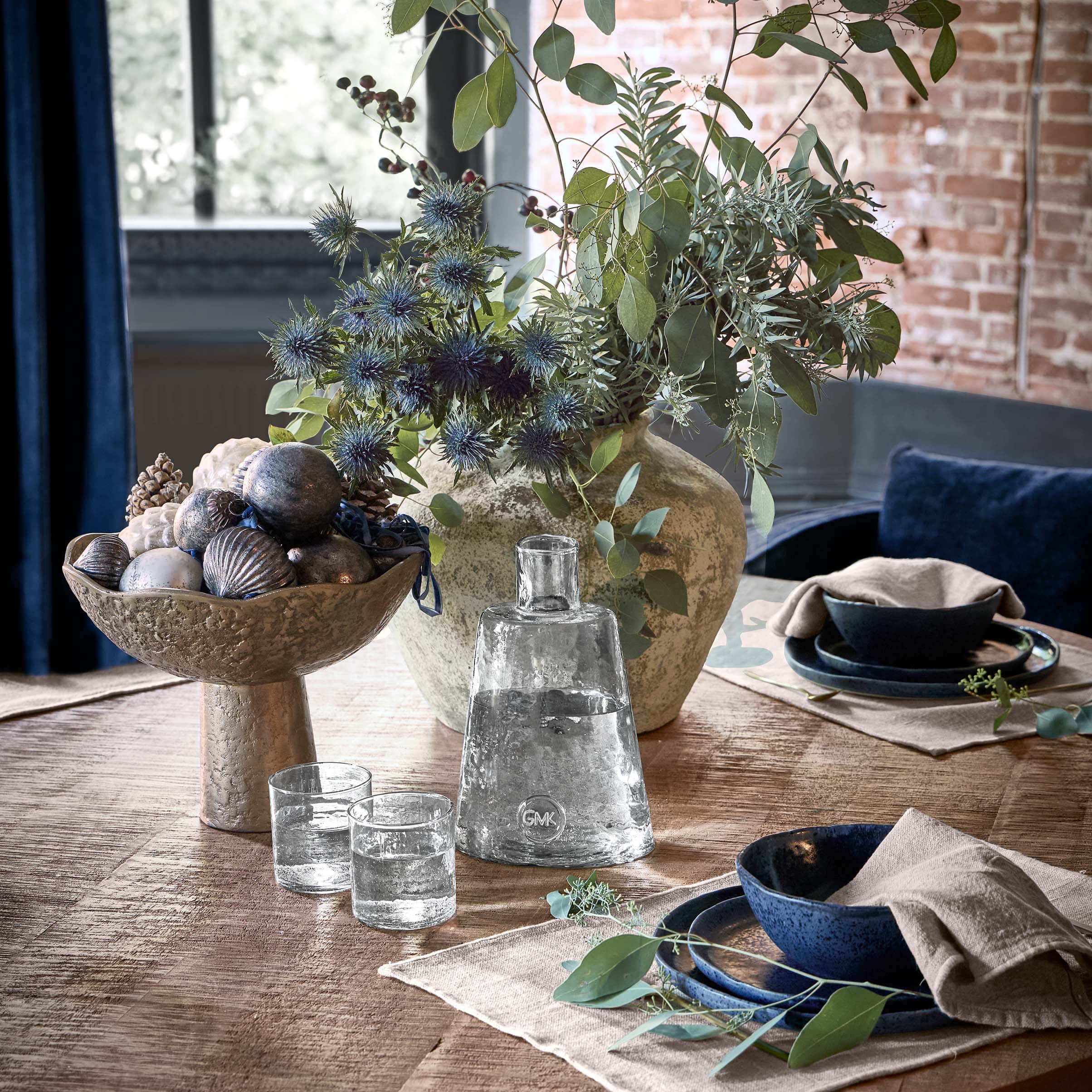 Dekorative Metallschale mit Zierobjekten und Vase mit grünen Blättern auf Holztisch im Wohnzimmer