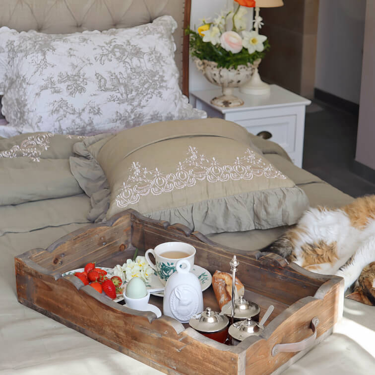 Holztablett auf Bett mit Teetasse, Ei und Erdbeeren, gemütliches Schlafzimmer mit bestickten Kissen