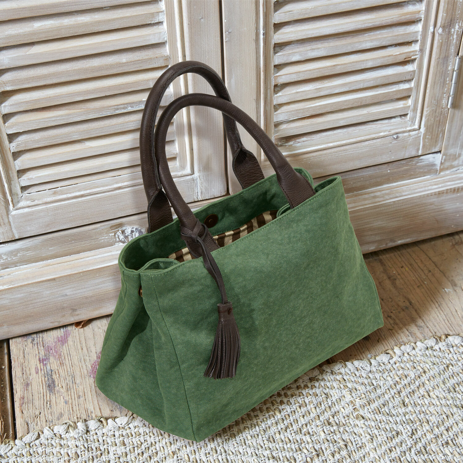 Tasche Hoya Grüne Stofftasche mit braunen Ledergriffen und Quaste auf hellem Holzboden.