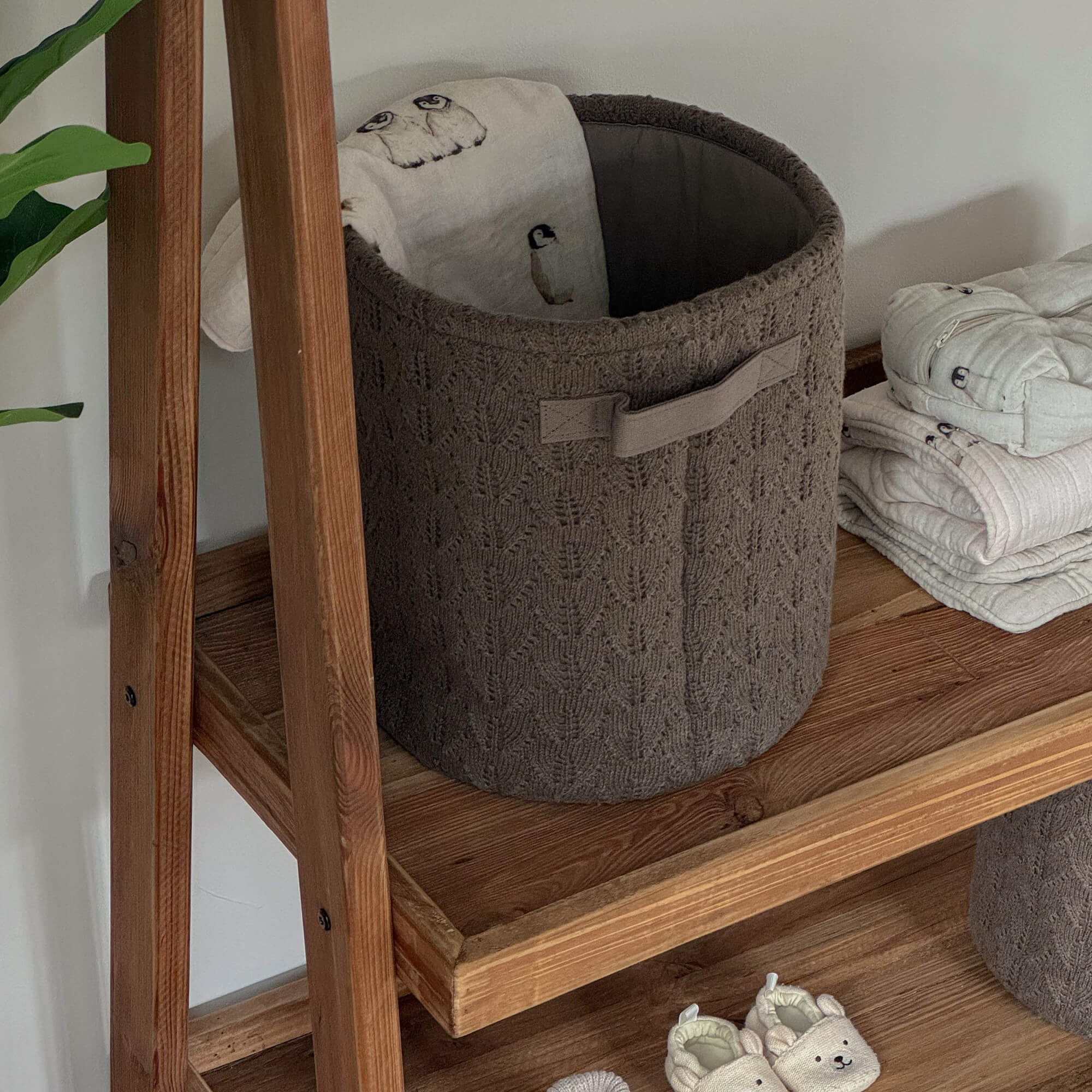 Brauner gestrickter Aufbewahrungskorb auf Holzregal mit weichem Stoff und Babyschuhen