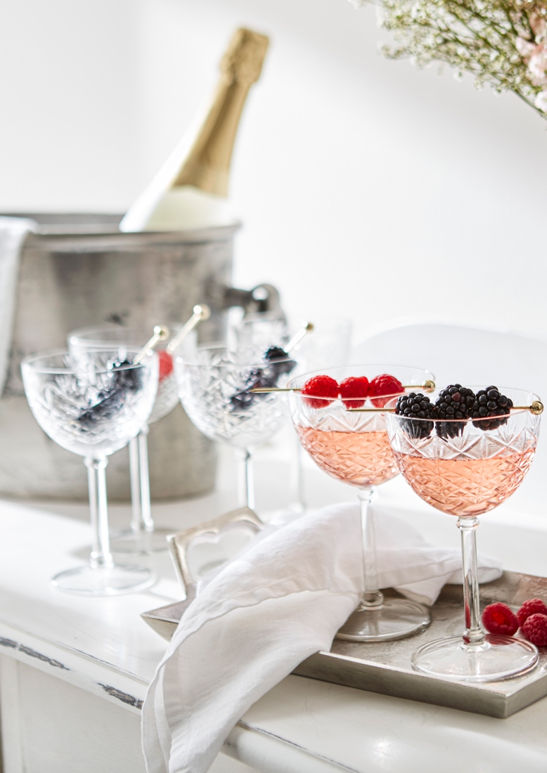 Kristallgläser mit rosafarbenem Getränk und Beeren auf silbernem Tablett, Eisbehälter und Flasche im Hintergrund