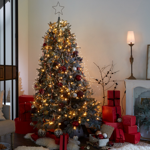Beleuchteter Weihnachtsbaum mit roten und silbernen Kugeln sowie roten Geschenken im gemütlichen Wohnzimmer