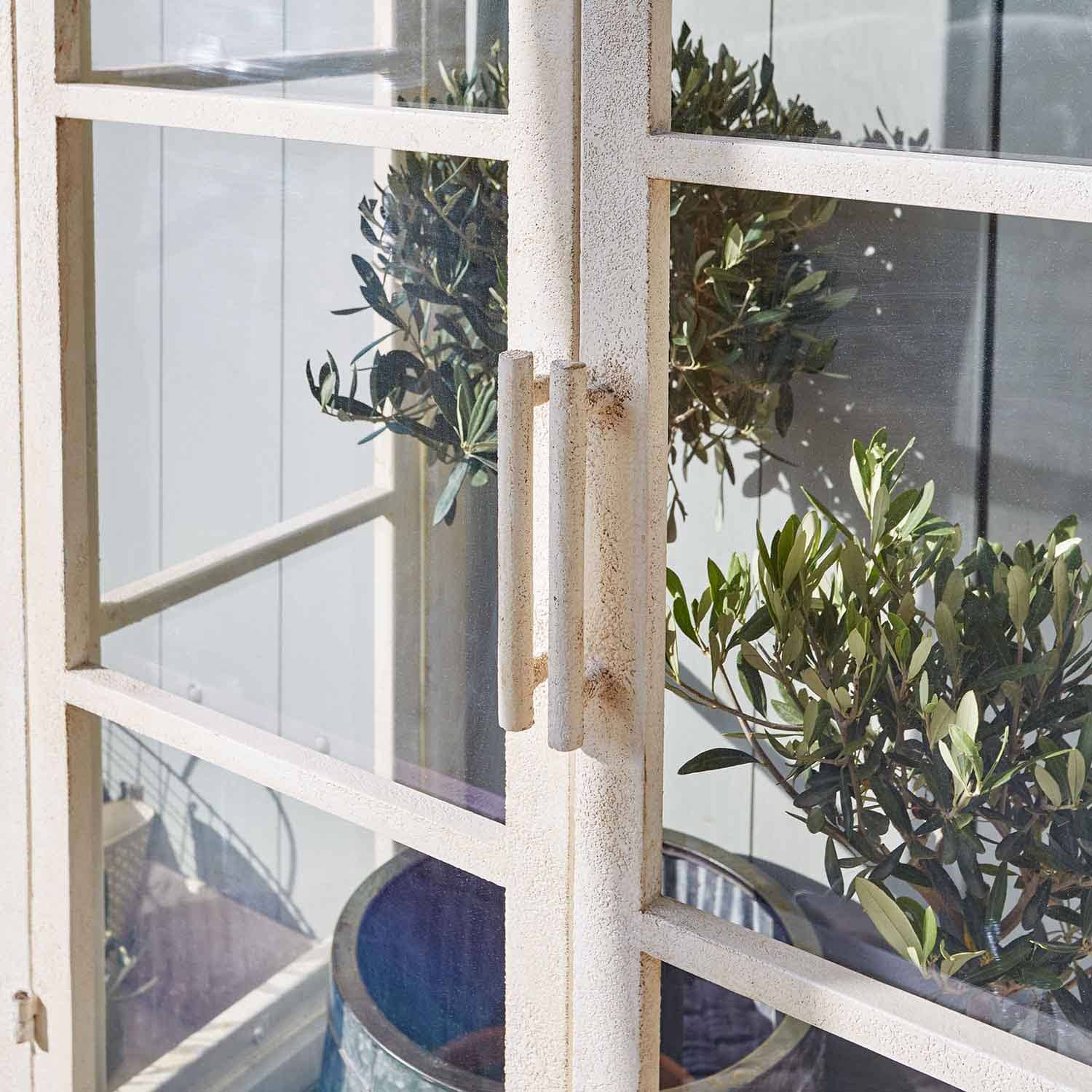 Weisse Metalltür mit Griffen und grünen Pflanzen im Hintergrund, Gartendekoration