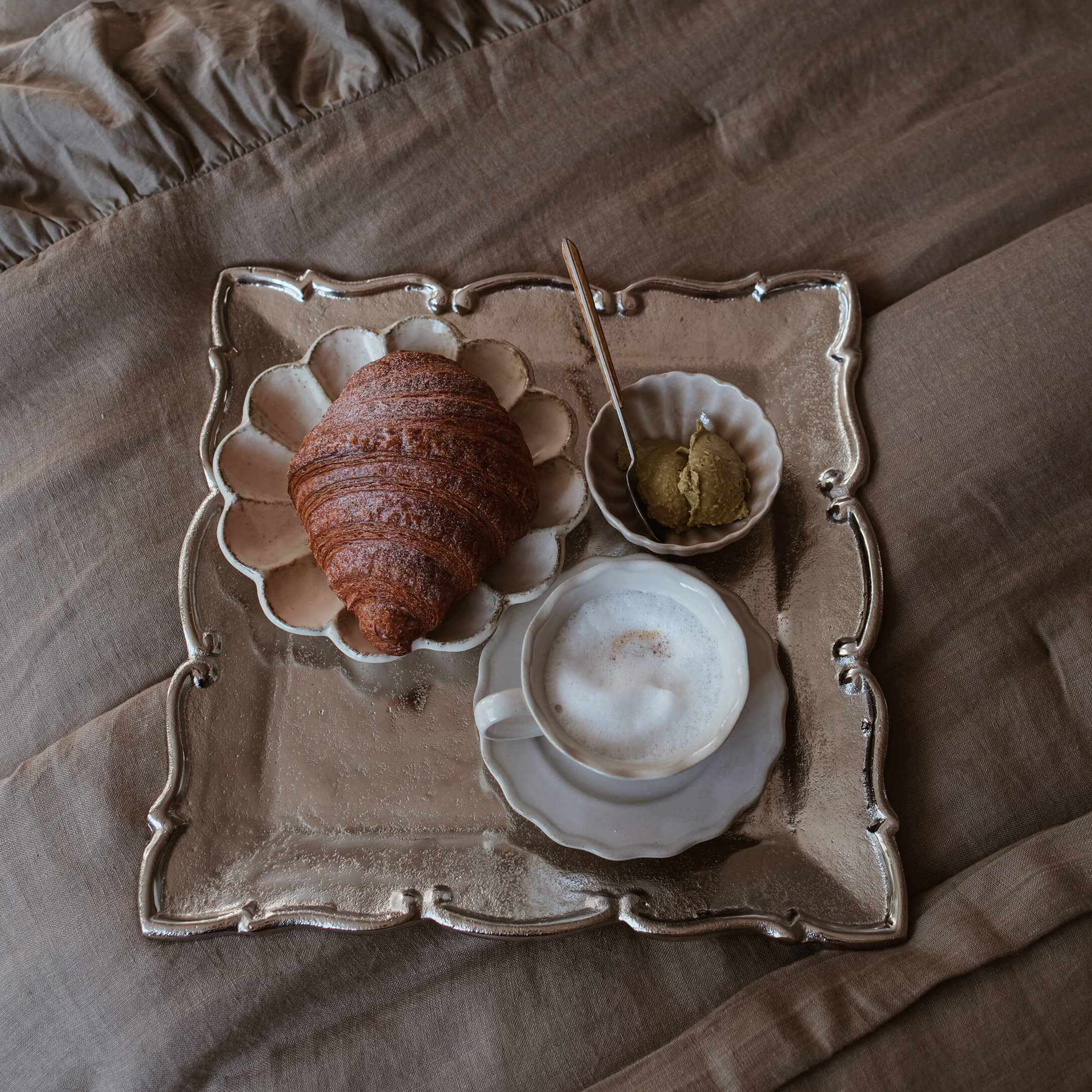 Tablett mit Gipfeli, Milchschaumkaffee und Aufstrich auf beigem Stoff im Slow-Living-Stil