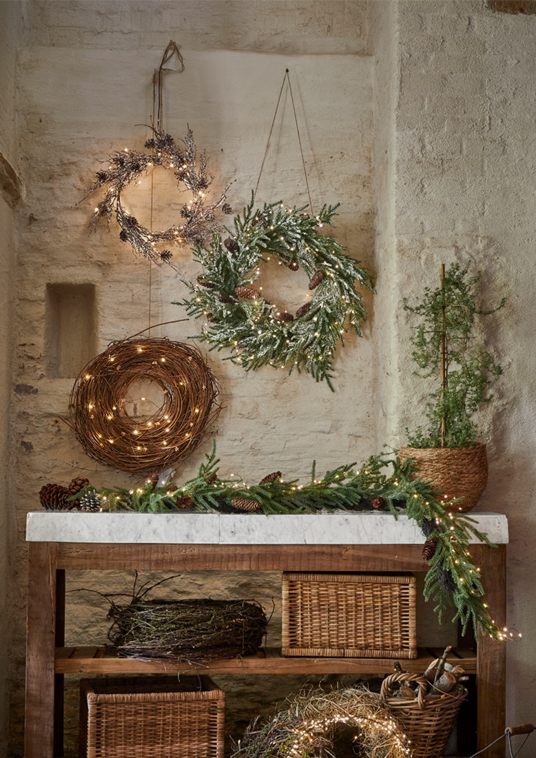 Weihnachtliche Dekokränze aus Zweigen und Lichterketten an Steinwand und Holztisch mit Marmorplatte