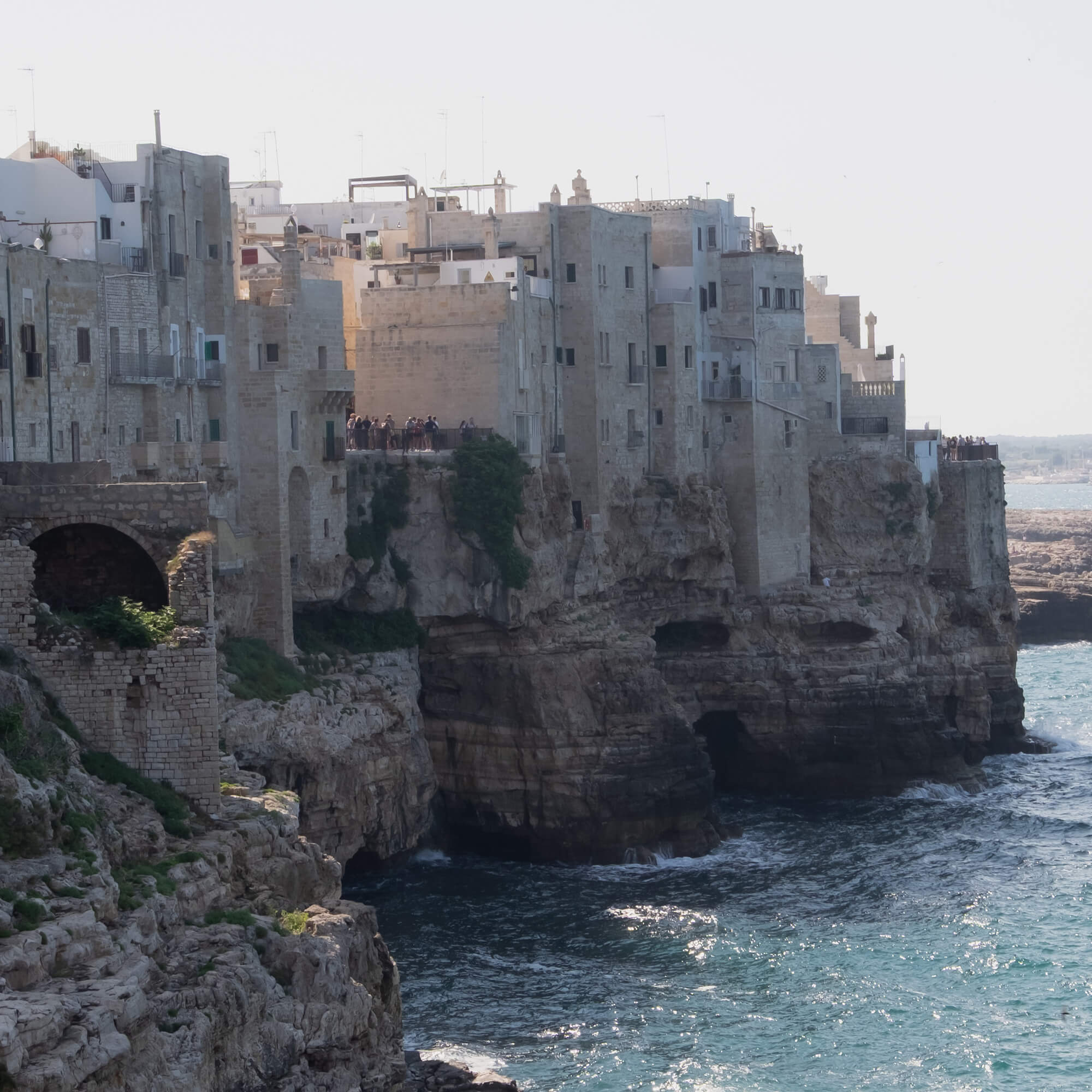 Alte steinerne Gebäude auf einer Klippe über dem Meer mit türkisfarbenem Wasser und Felsen darunter.
