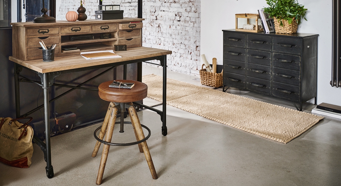 Schreibtisch aus Holz und Metall mit vielen Schubladen und braunem Lederhocker im Industriestil
