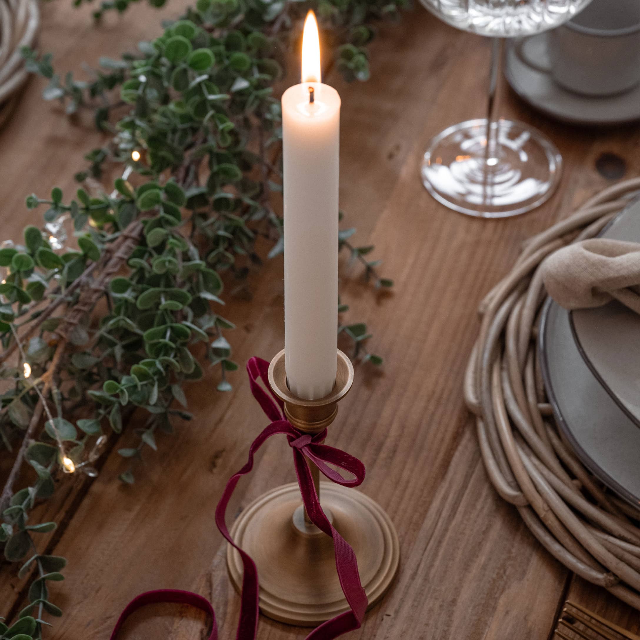 Goldener Kerzenhalter mit weisser Kerze und rotem Samtband auf Holztisch mit Weihnachtsdekoration