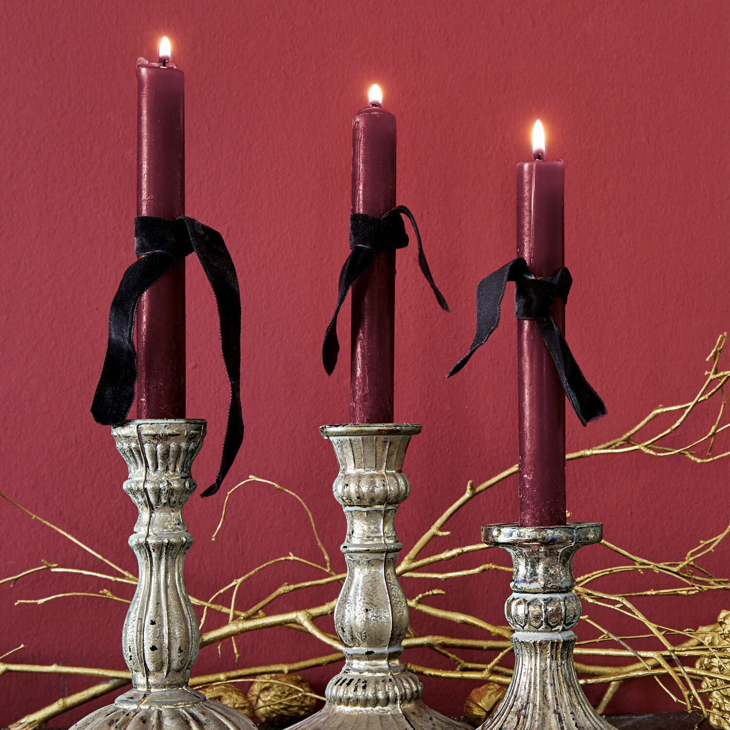 Kerze 12er Set Bauceau Drei silberne Metallkerzenhalter mit bordeauxroten Kerzen und schwarzen Bändern vor rotem Hintergrund