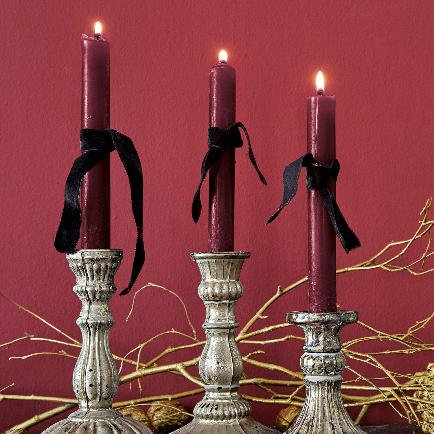 Kerze 12er Set Bauceau Drei silberne Metallkerzenhalter mit bordeauxroten Kerzen und schwarzen Bändern vor rotem Hintergrund