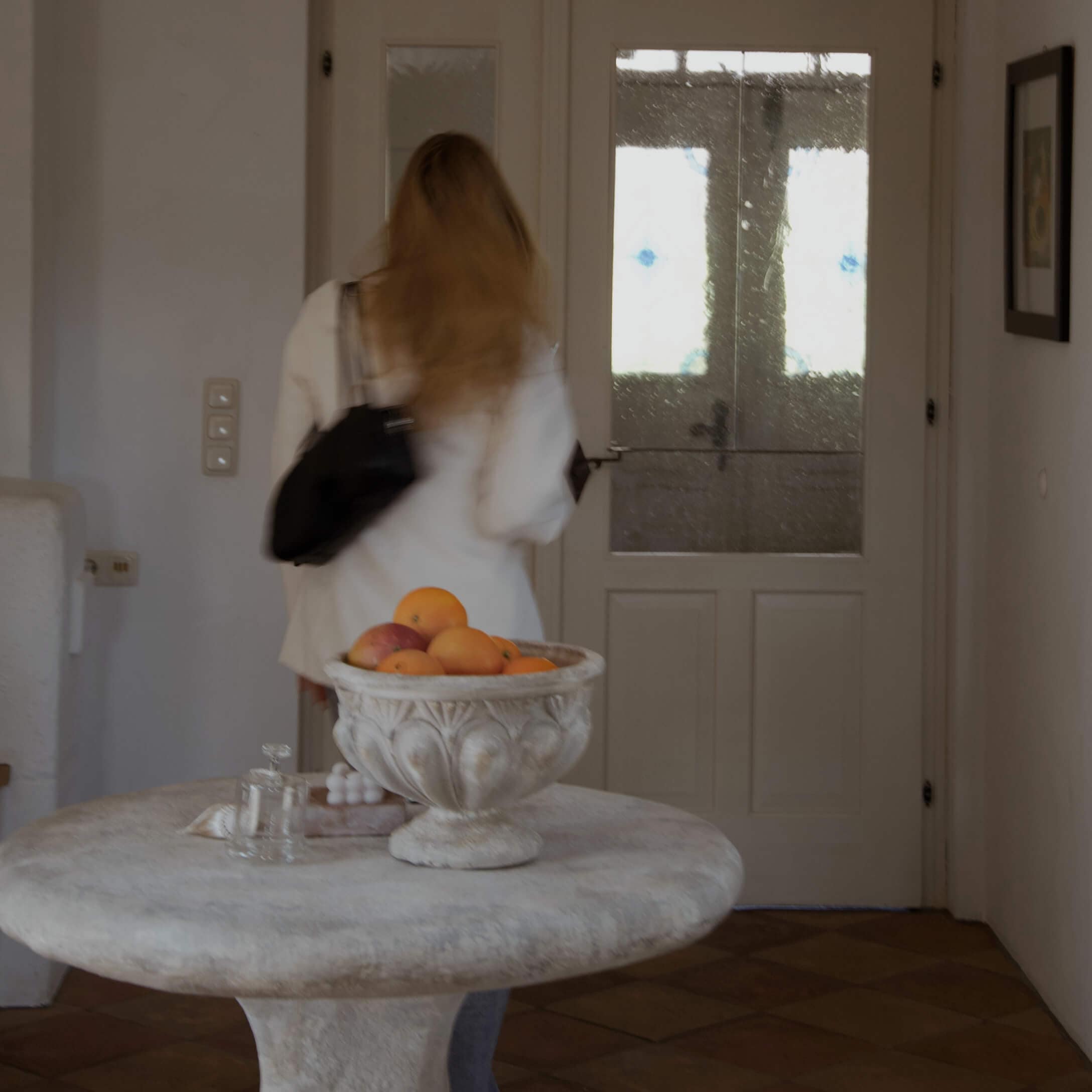 Dekorative Steinschale mit Orangen auf rundem Tisch in hellem Raum mit Glastür.