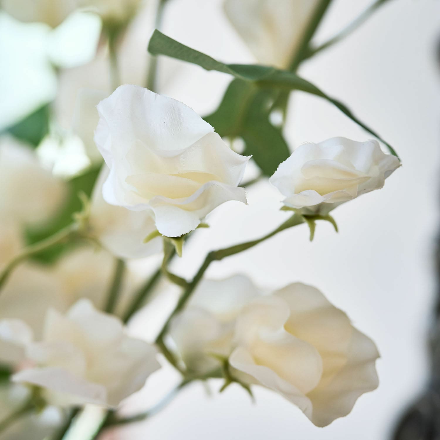 Zarte weisse Stoffblumen mit grünen Stielen als dekorative Innenraumgestaltung