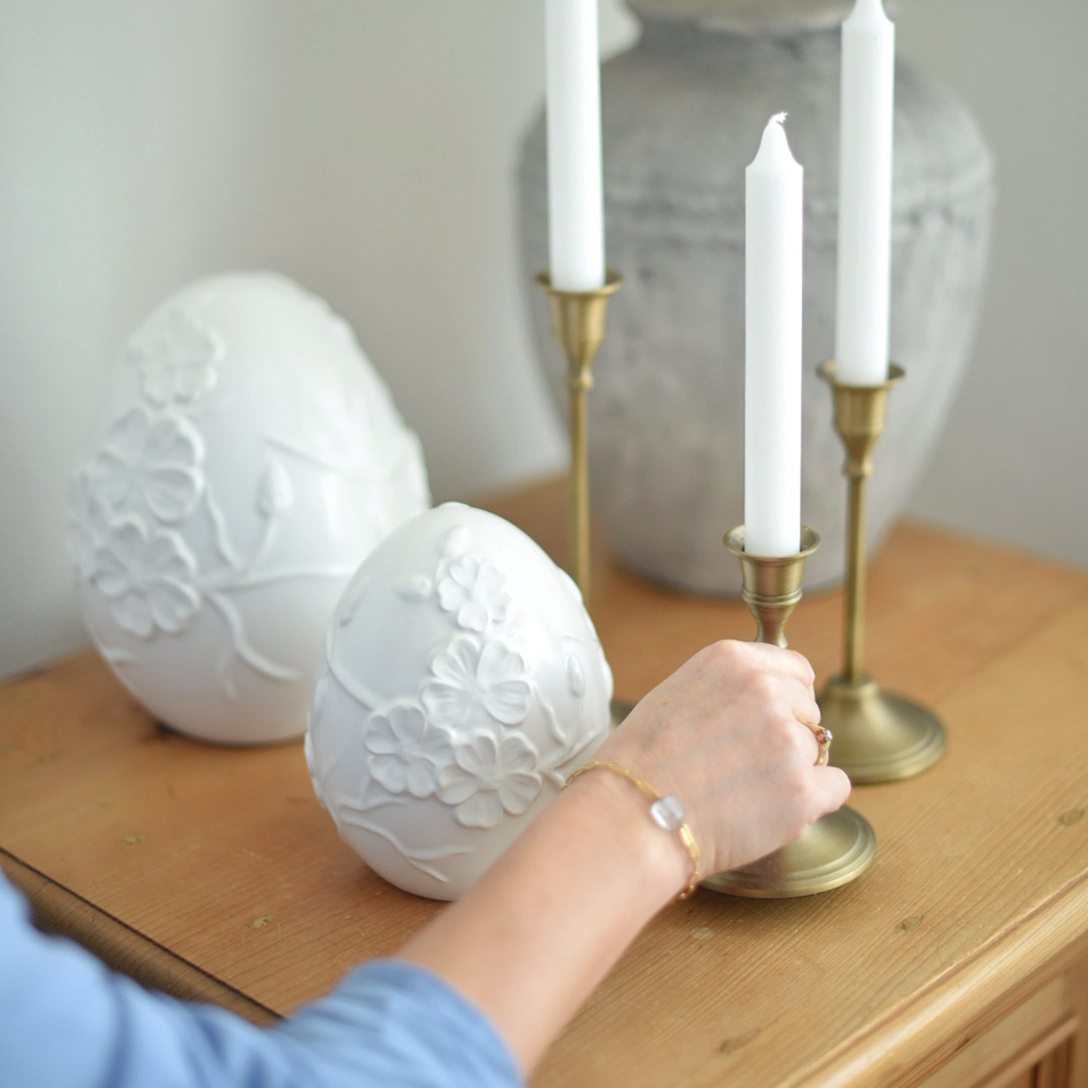Weiße Keramik-Eier mit Blumenrelief auf Holztisch neben Messing-Kerzenhaltern