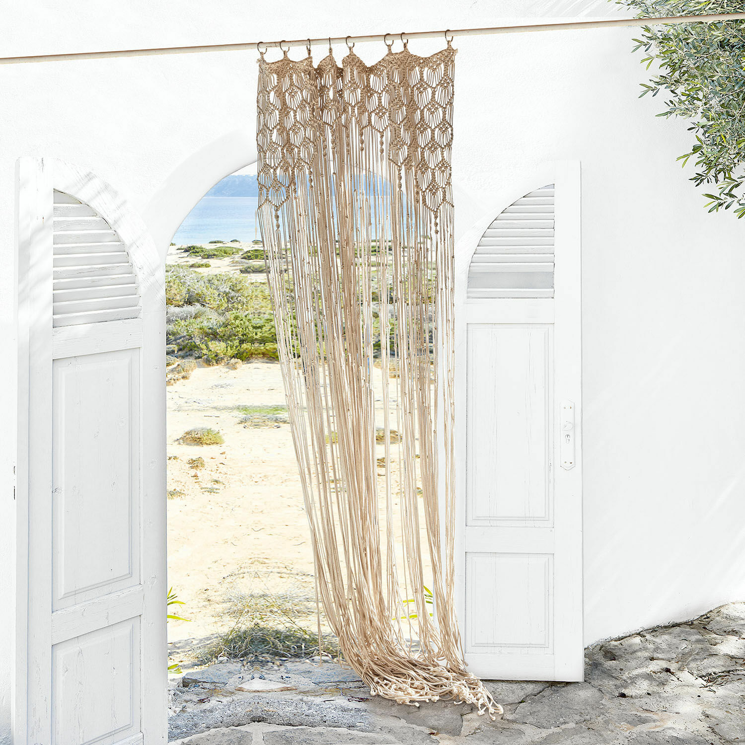Gardine Manville Beige Baumwollmakramee an weissem offenem Tor mit Blick auf Strand und Meer