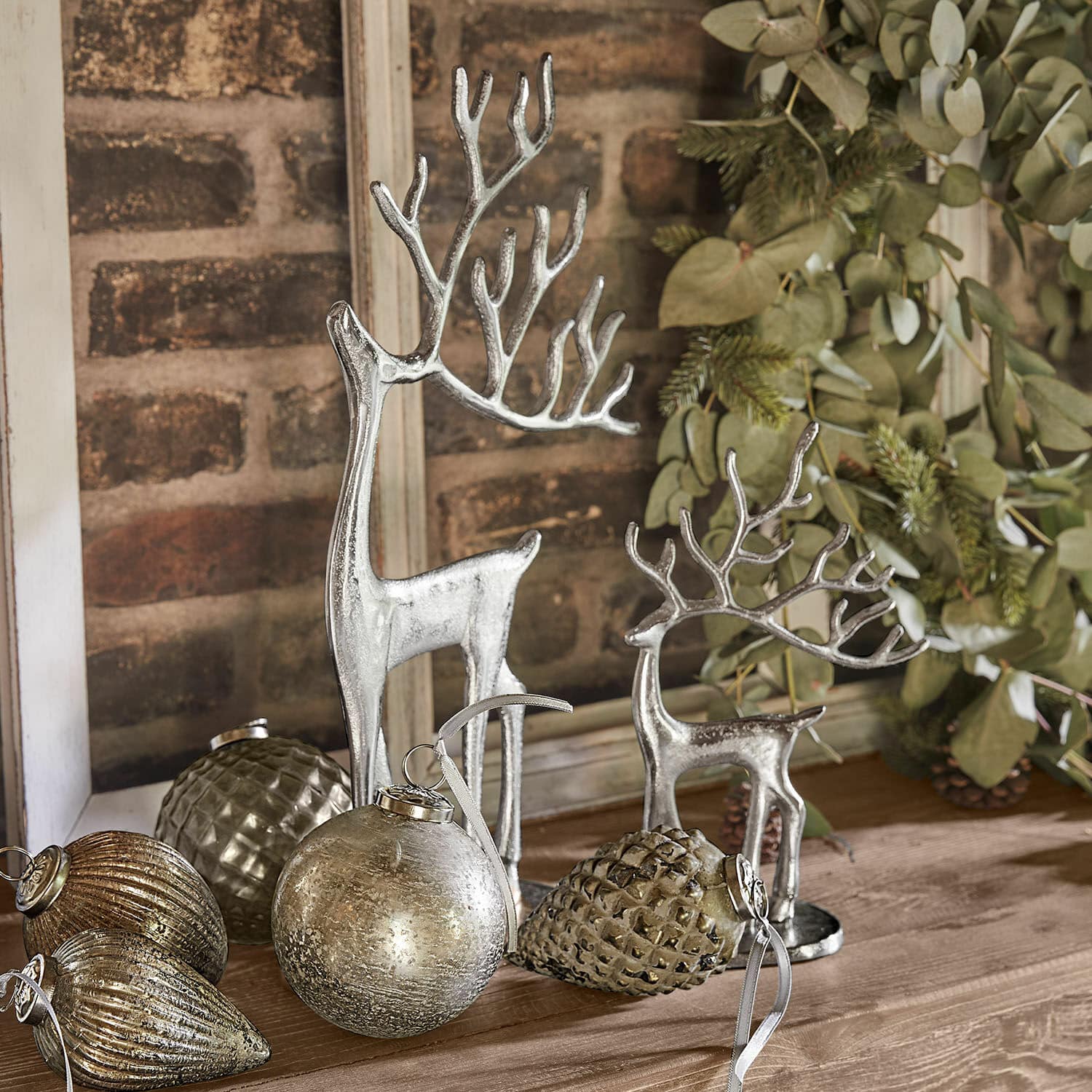 Deko-Rentier 2er Set Zerlay Silberne Rentierfiguren und Weihnachtsdekorationen auf Holztisch mit grünen Zweigen arrangiert