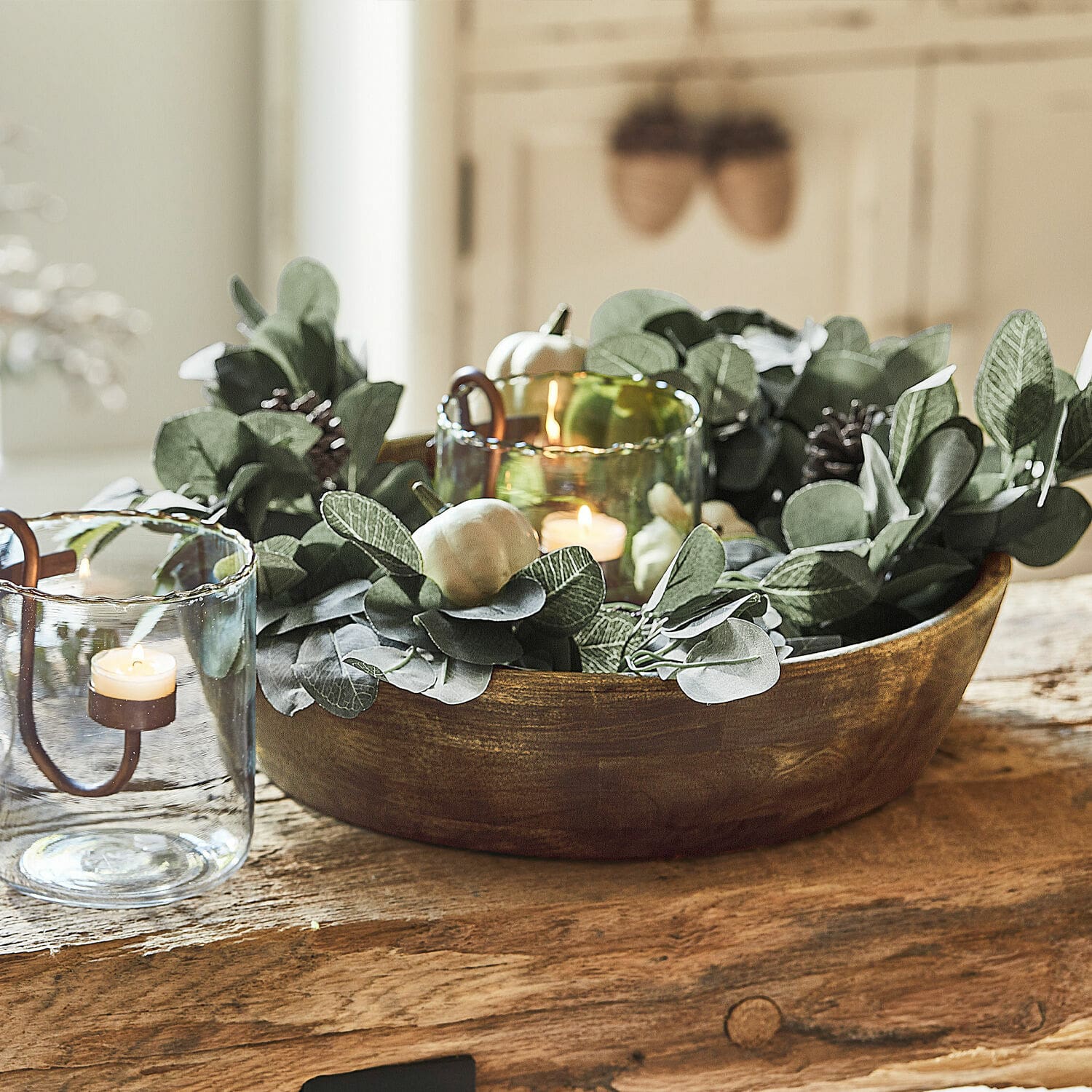 Girlande Belfays Dekorative Holzschale mit grünen Blättern und Kerzen in Glaswindlichtern auf Holztisch
