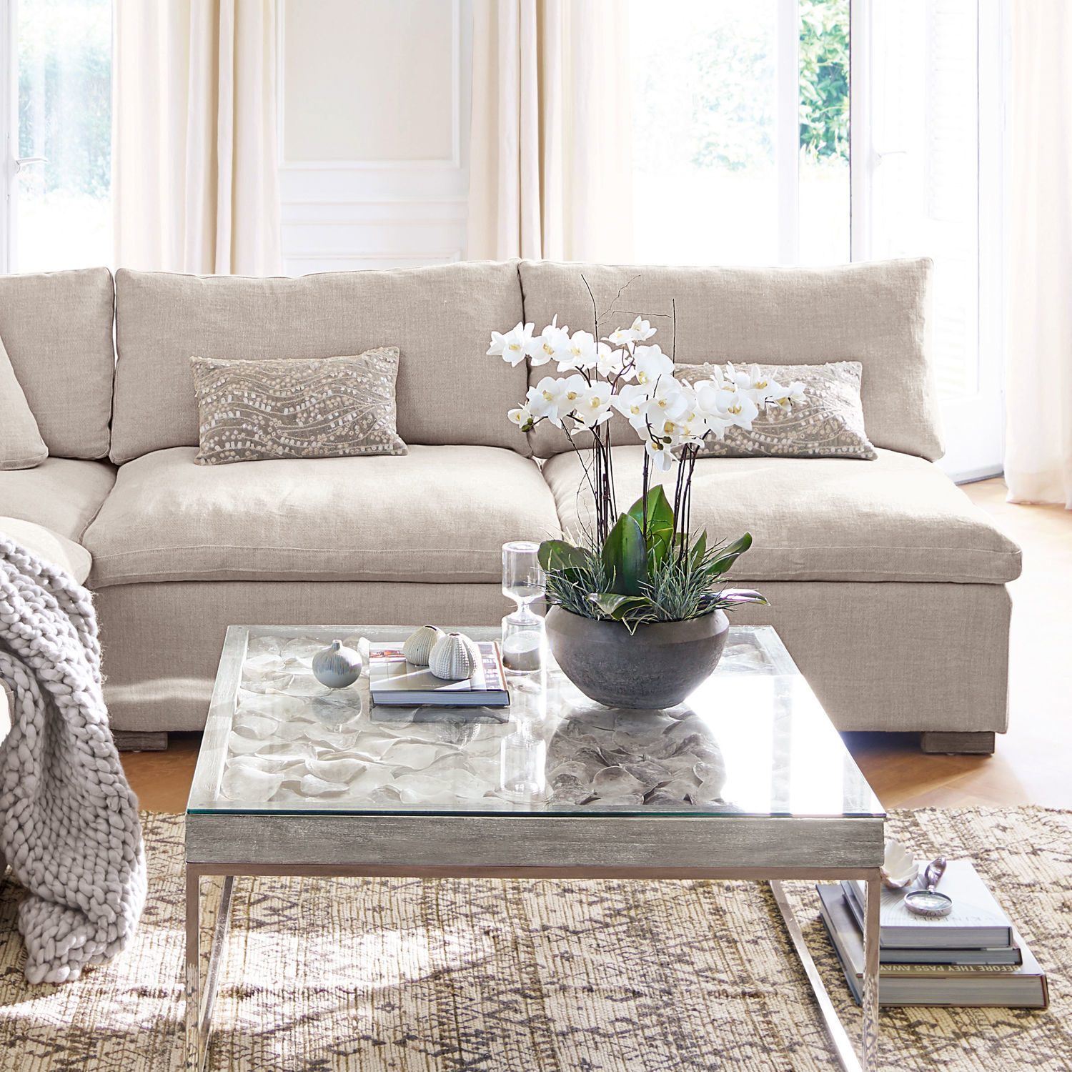 Sessel Bennington Beiges Stoffsofa mit dekorativen Kissen und Glastisch mit weisser Blume im Wohnzimmer