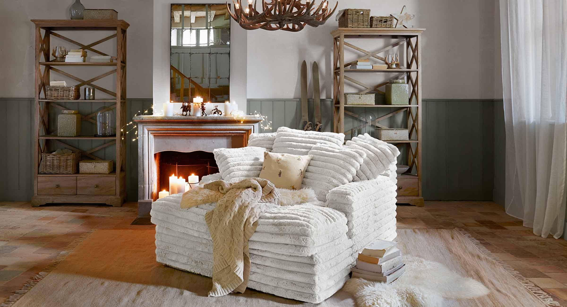 Gemütlicher weisser Sessel aus weichem Material im Chalet-Stil mit Kamin und Holzregalen im Wohnzimmer