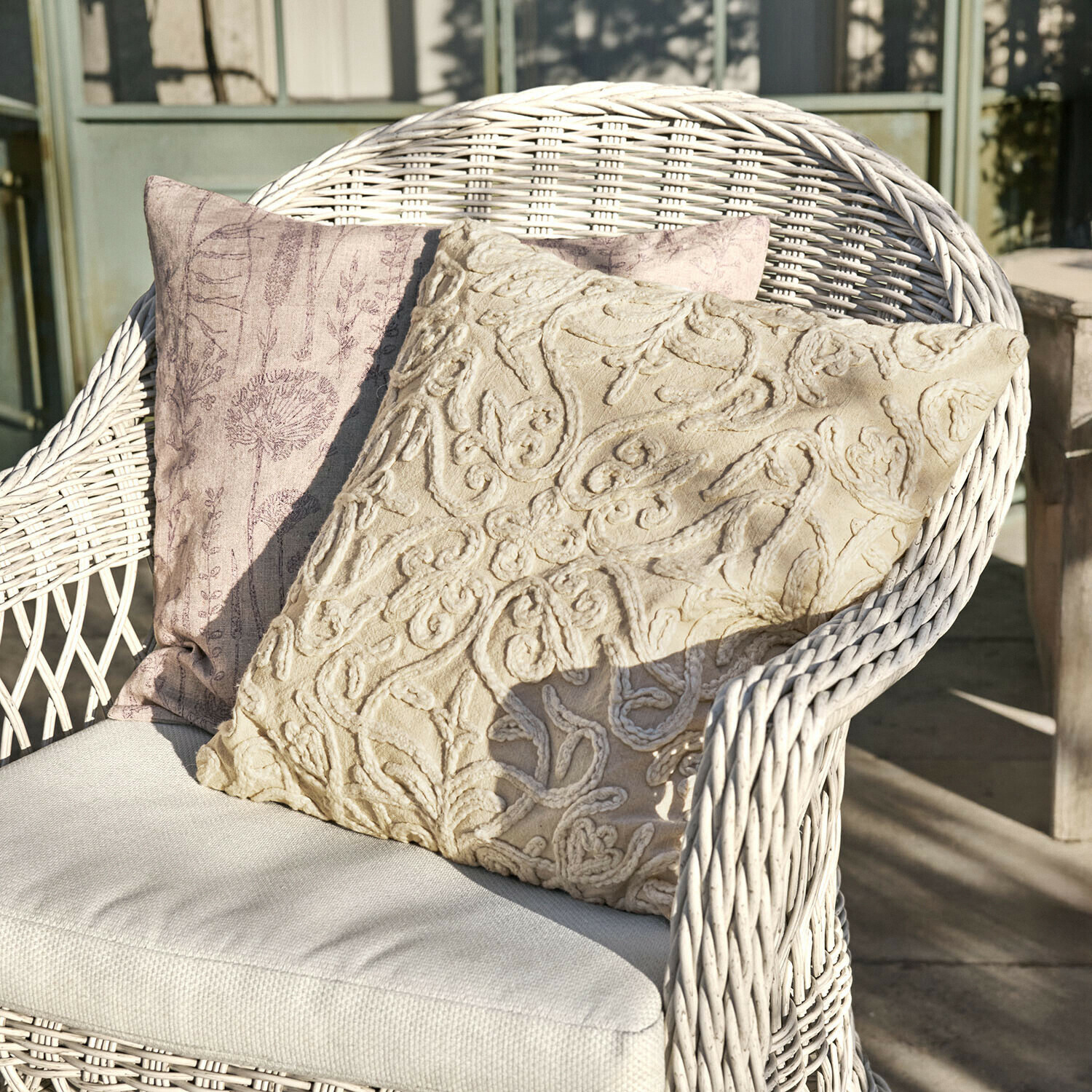 Kissenhülle 2er Set Floraine Zwei dekorative Kissen in Beige und Rosa auf einem weissen Korbsessel auf der Terrasse