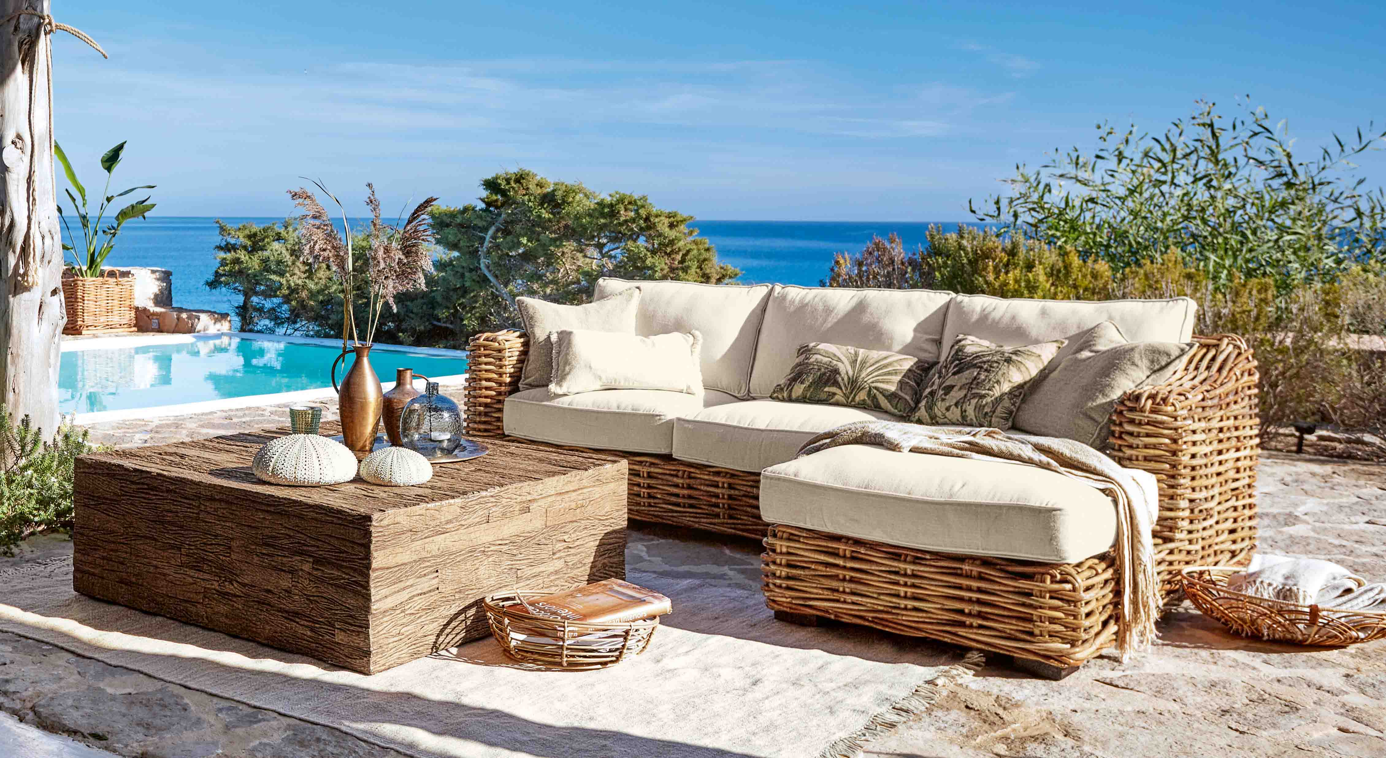 Rattan-Gartenmöbel mit cremefarbenen Polstern am Pool mit Meerblick