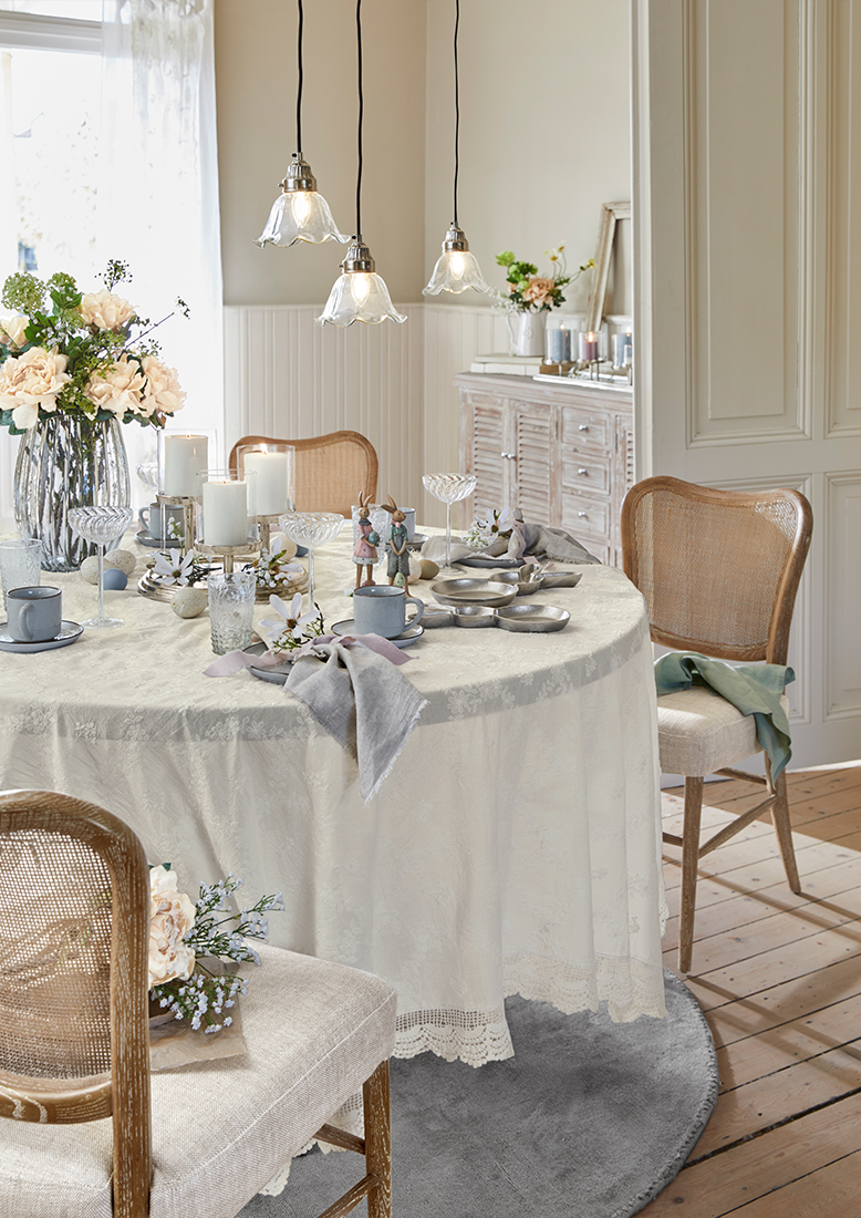 Eleganter Tisch mit cremefarbenem Tischtuch, Blumenarrangements und Kerzen in hellem, gemütlichem Raum