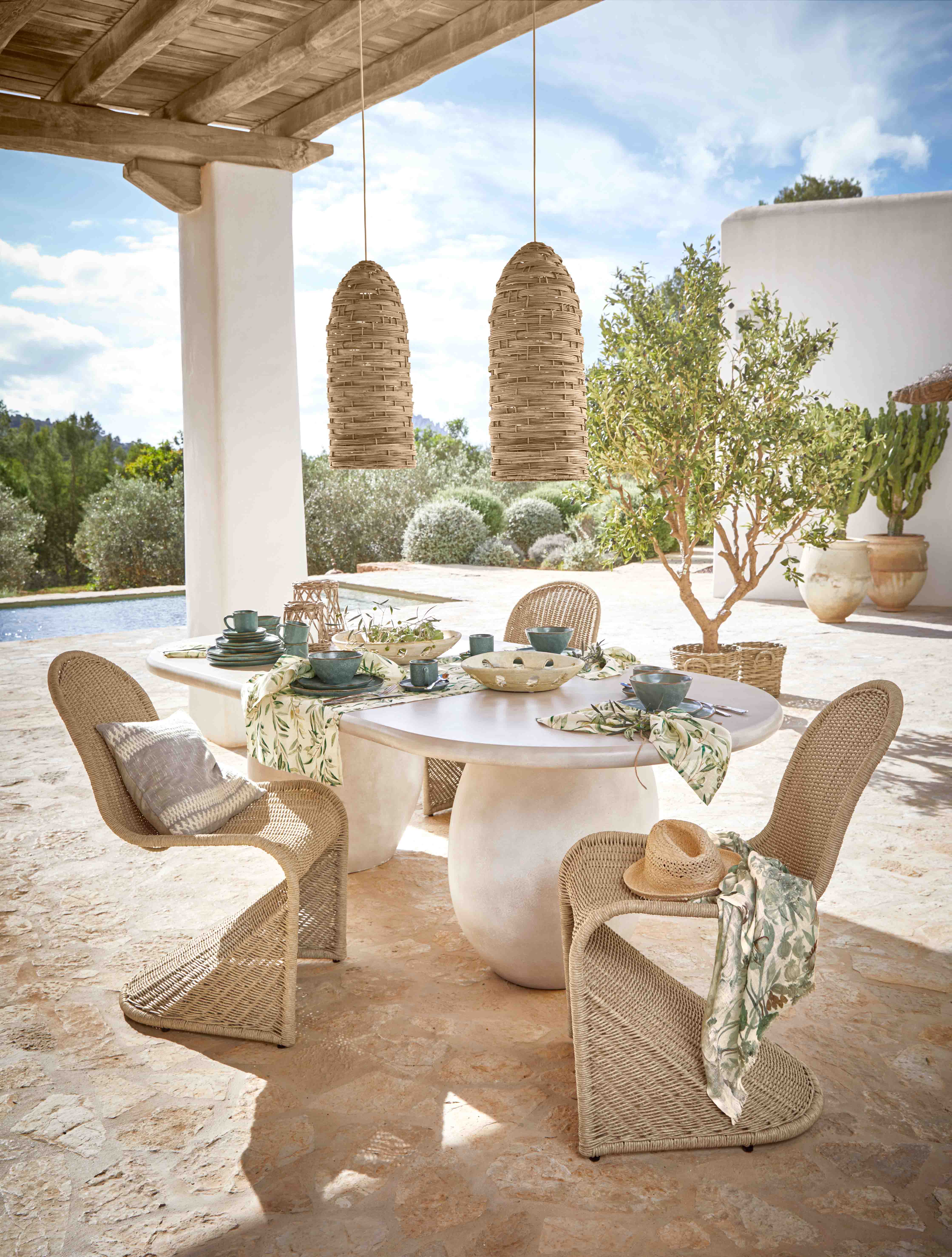 Gartenmöbel-Set mit geflochtenen Stühlen und weissem Tisch auf Terrasse mit Tischdekoration