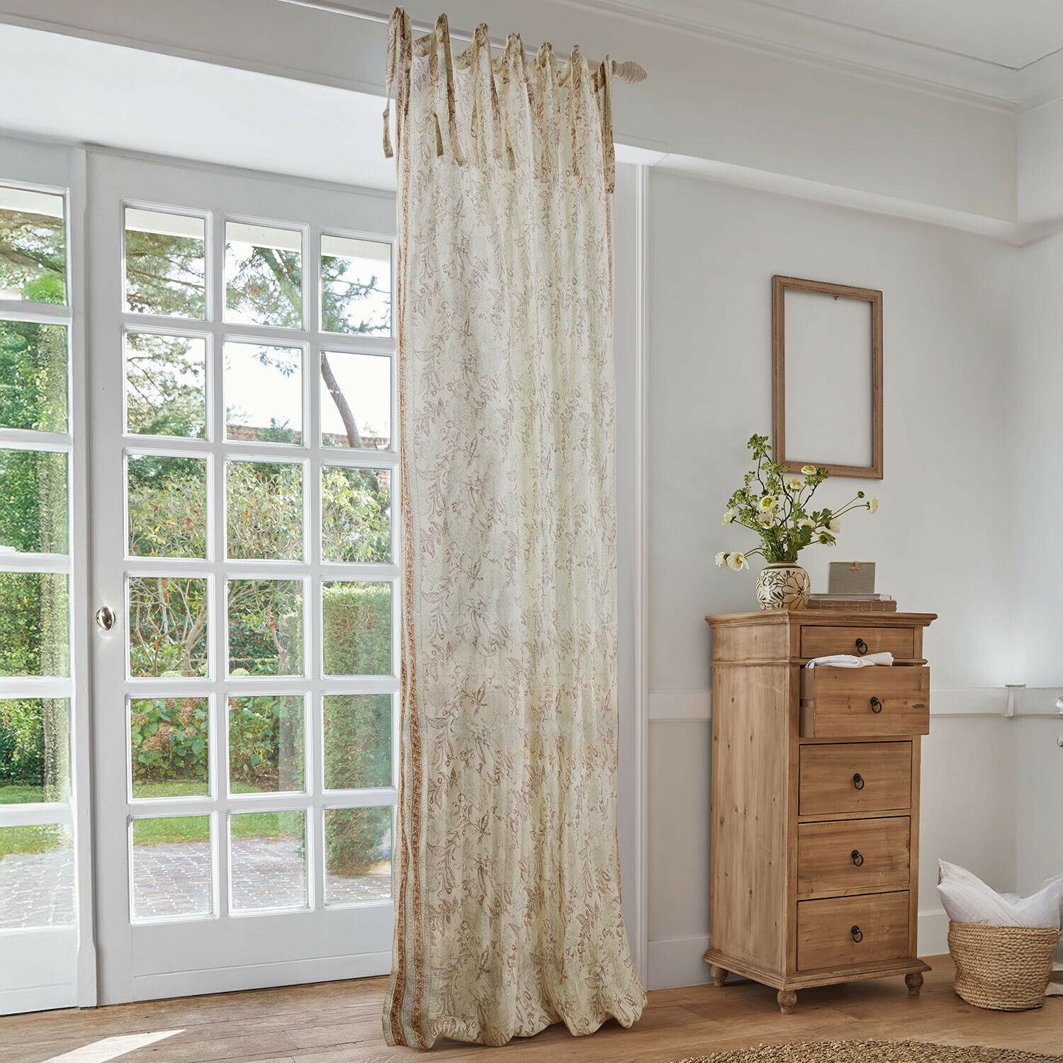 Gardine Floréane Beiger Vorhang mit feinem Blumenmuster in hellem Wohnzimmer mit Holzkommode und grossem Fenster