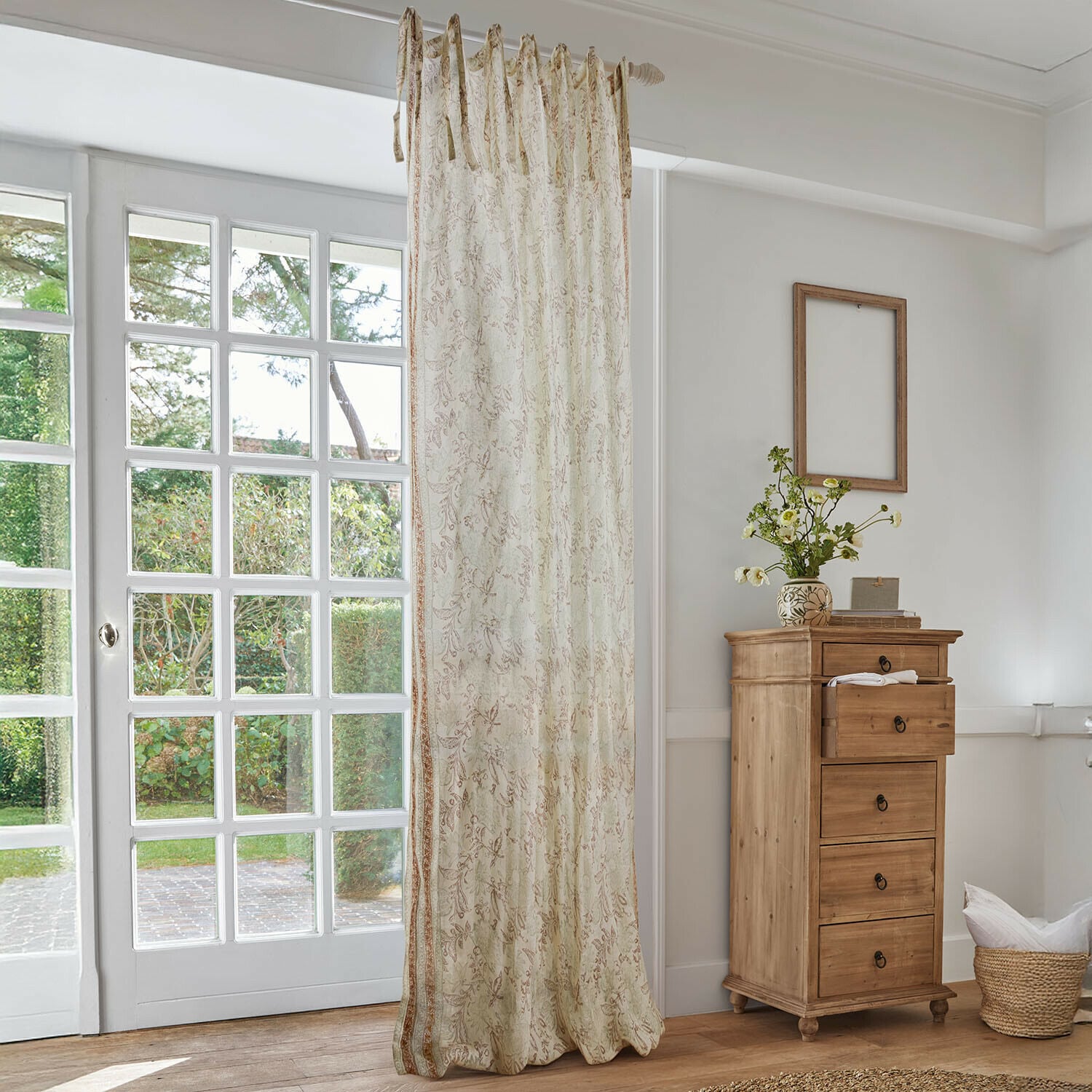 Gardine Floréane Beiger Vorhang mit feinem Blumenmuster in hellem Wohnzimmer mit Holzkommode und grossem Fenster